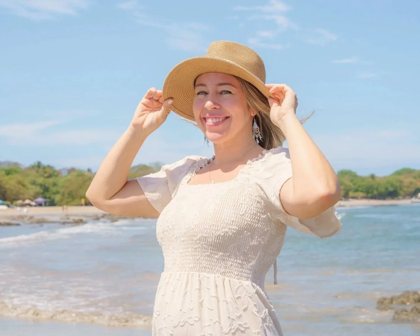 Dr. Ashley Lynch, EMDR therapist in CA, smiling on the beach wearing a hat and a light-colored dress.