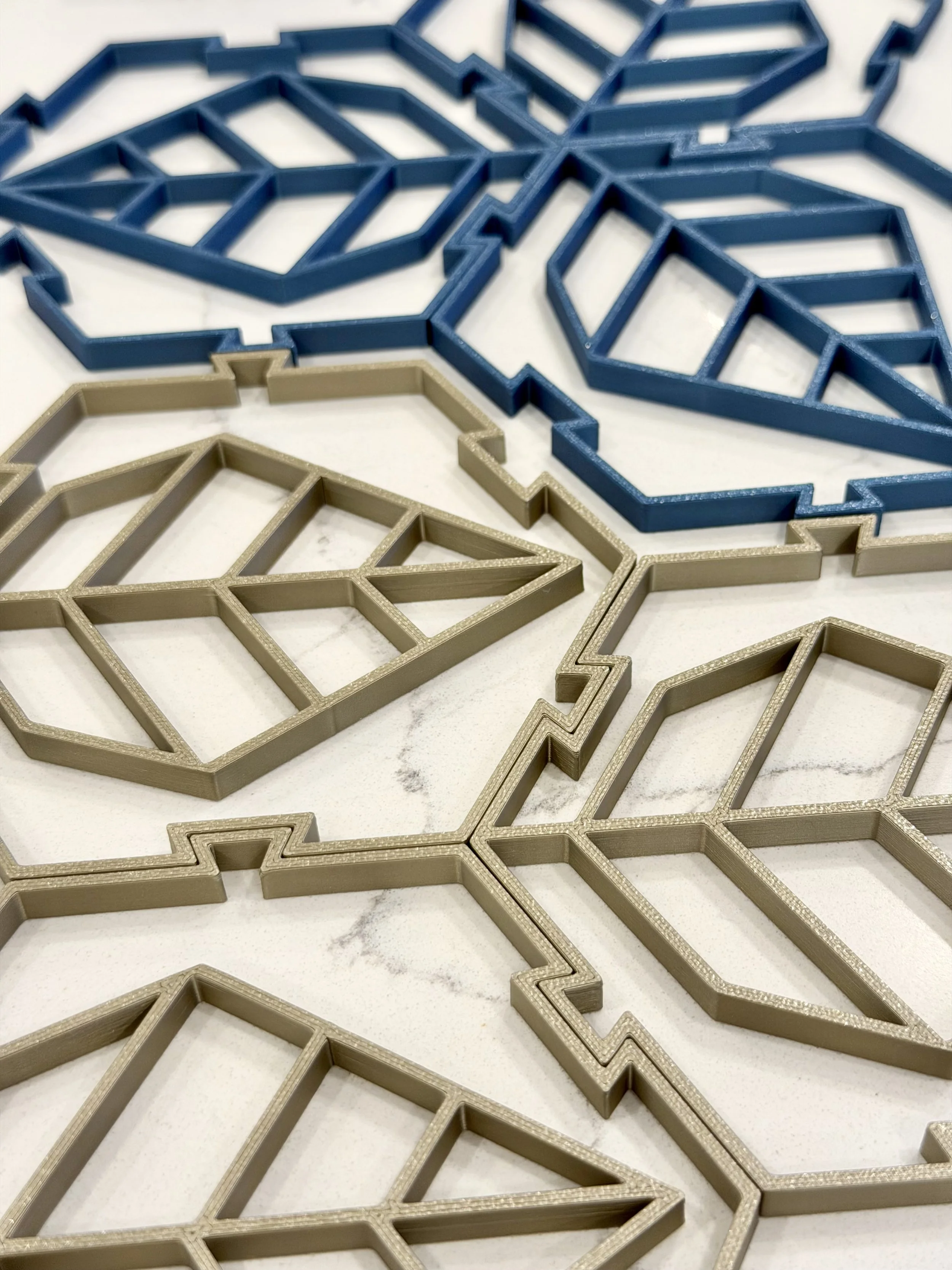 Close-up view of several geometric-shaped cookie cutters in gold and blue colors, arranged on a white surface.