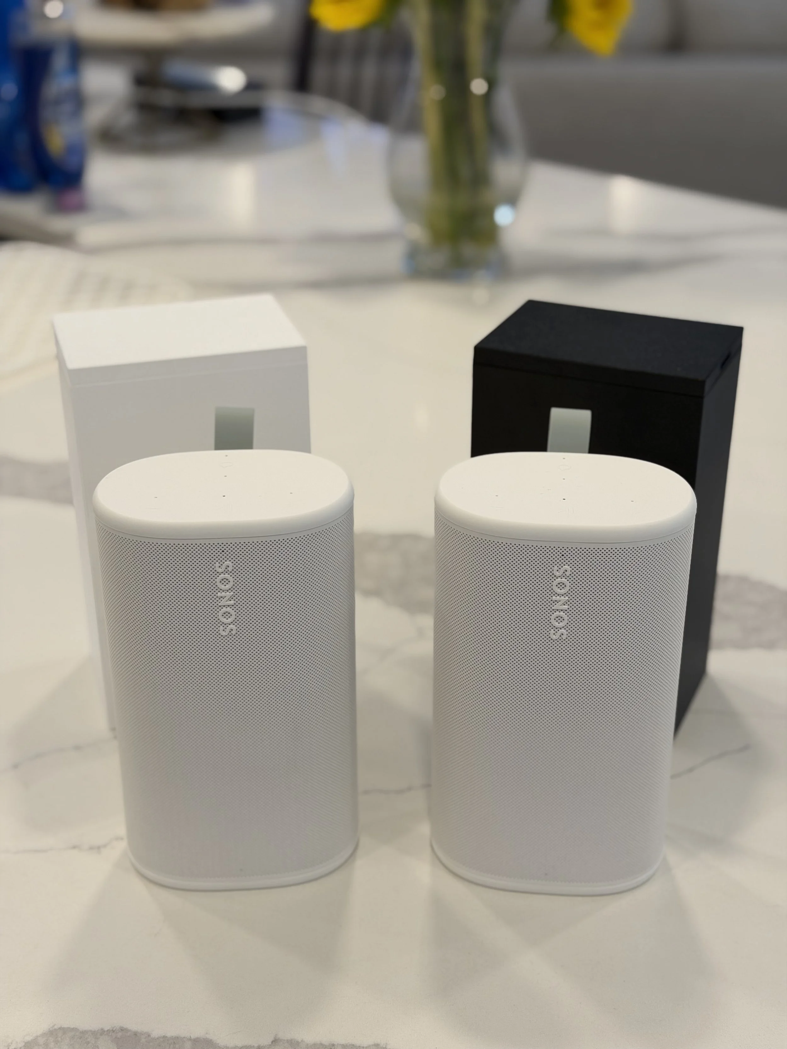 Two white Sony smart speakers and two black audio boxes placed on a white surface.