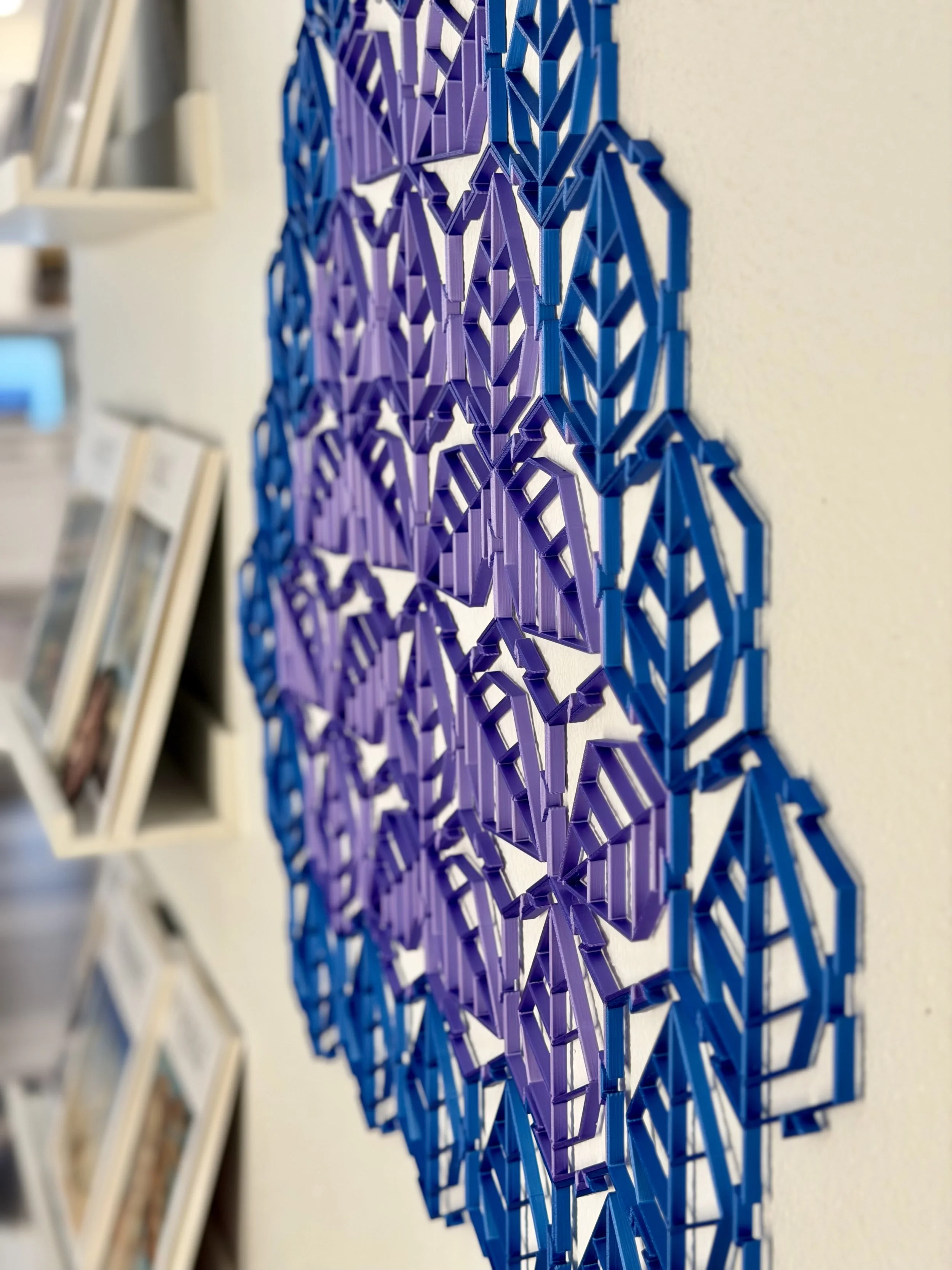 Colorful geometric wall art hanging with purple and blue shapes on a white wall.