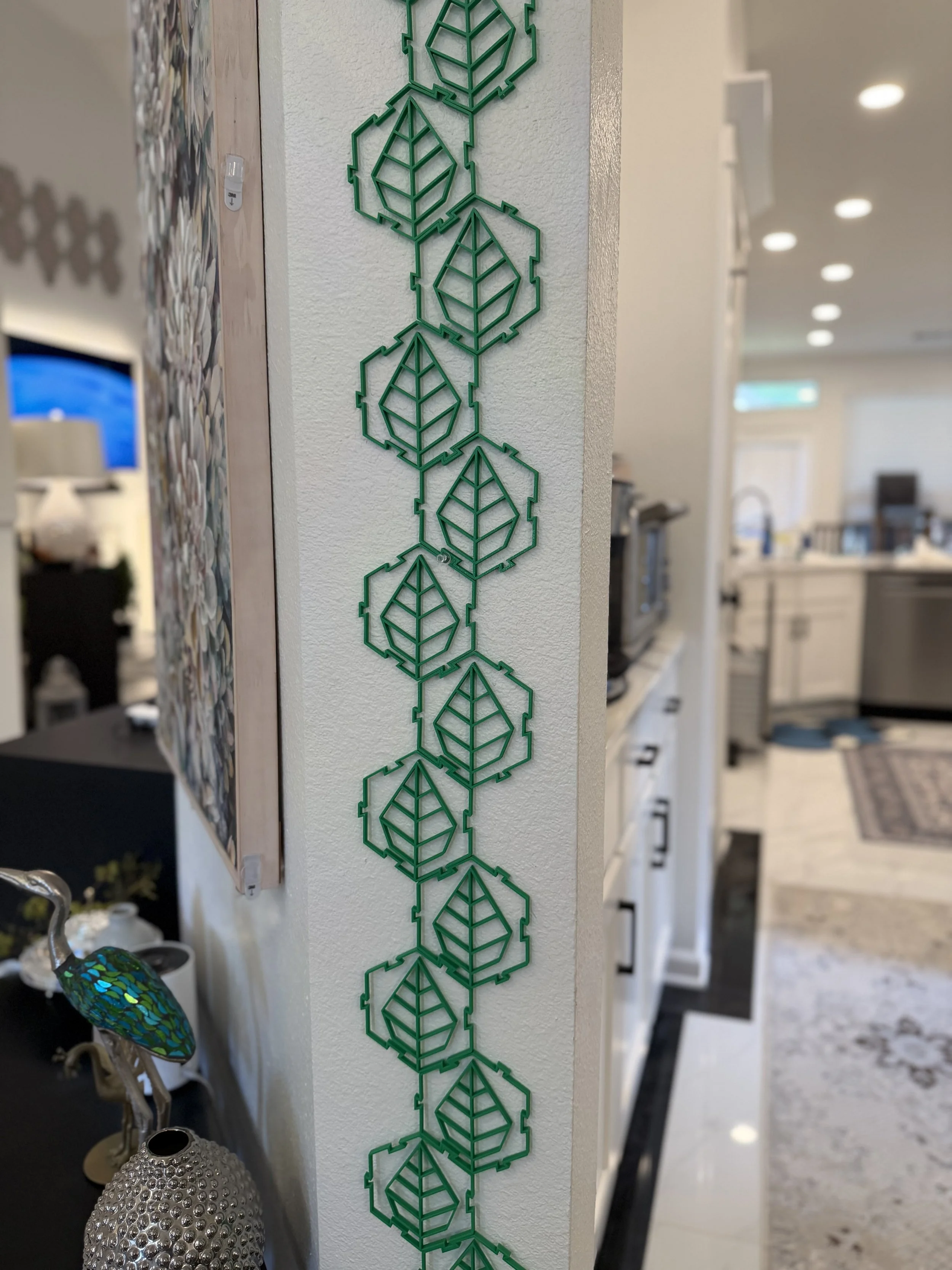 A vertical row of green metal decorative leaves on a wall in a room.