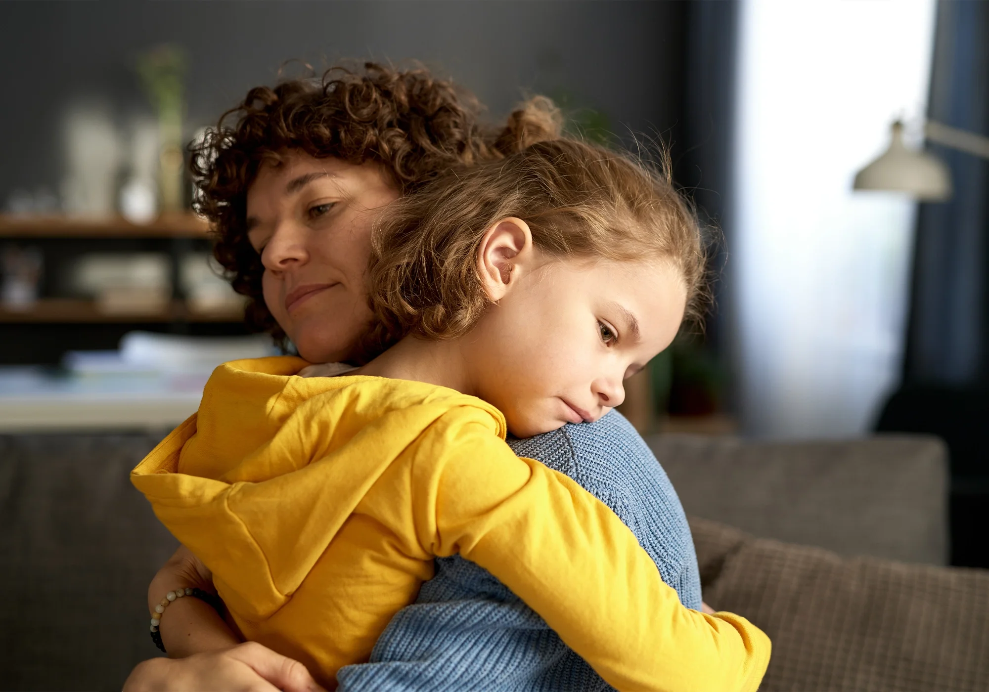 Child resting on a parent’s shoulder with a quiet, concerned expression
