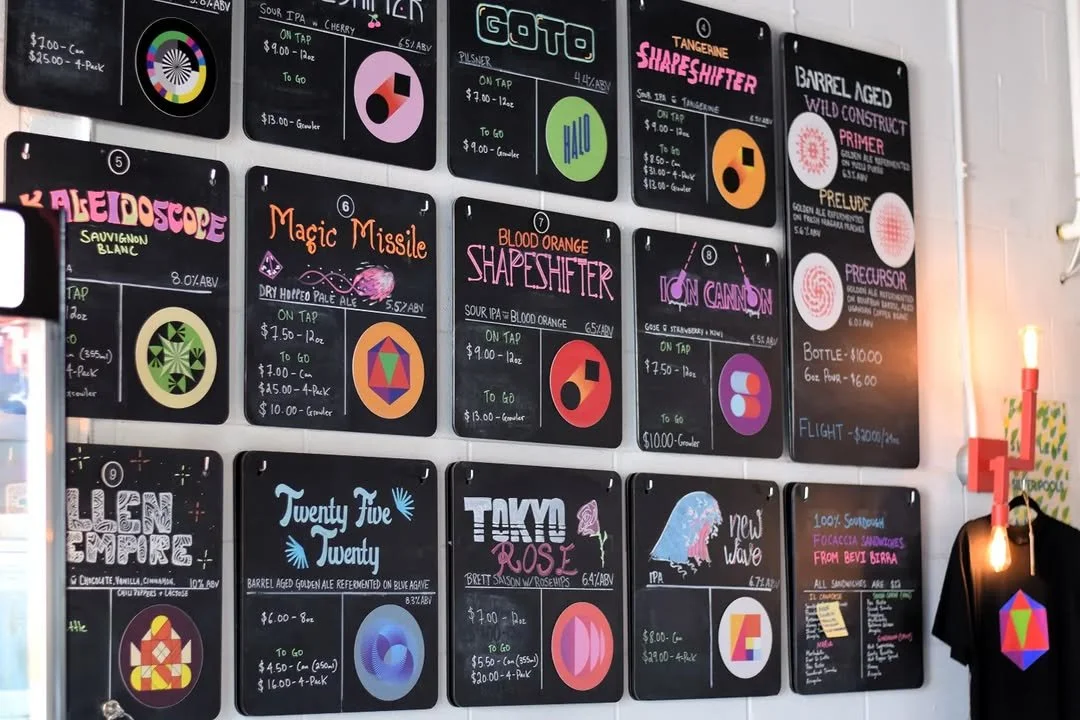 Menu boards displaying various craft beers, their names, styles, prices, and alcohol content, arranged on a wall in a brewery or bar setting.