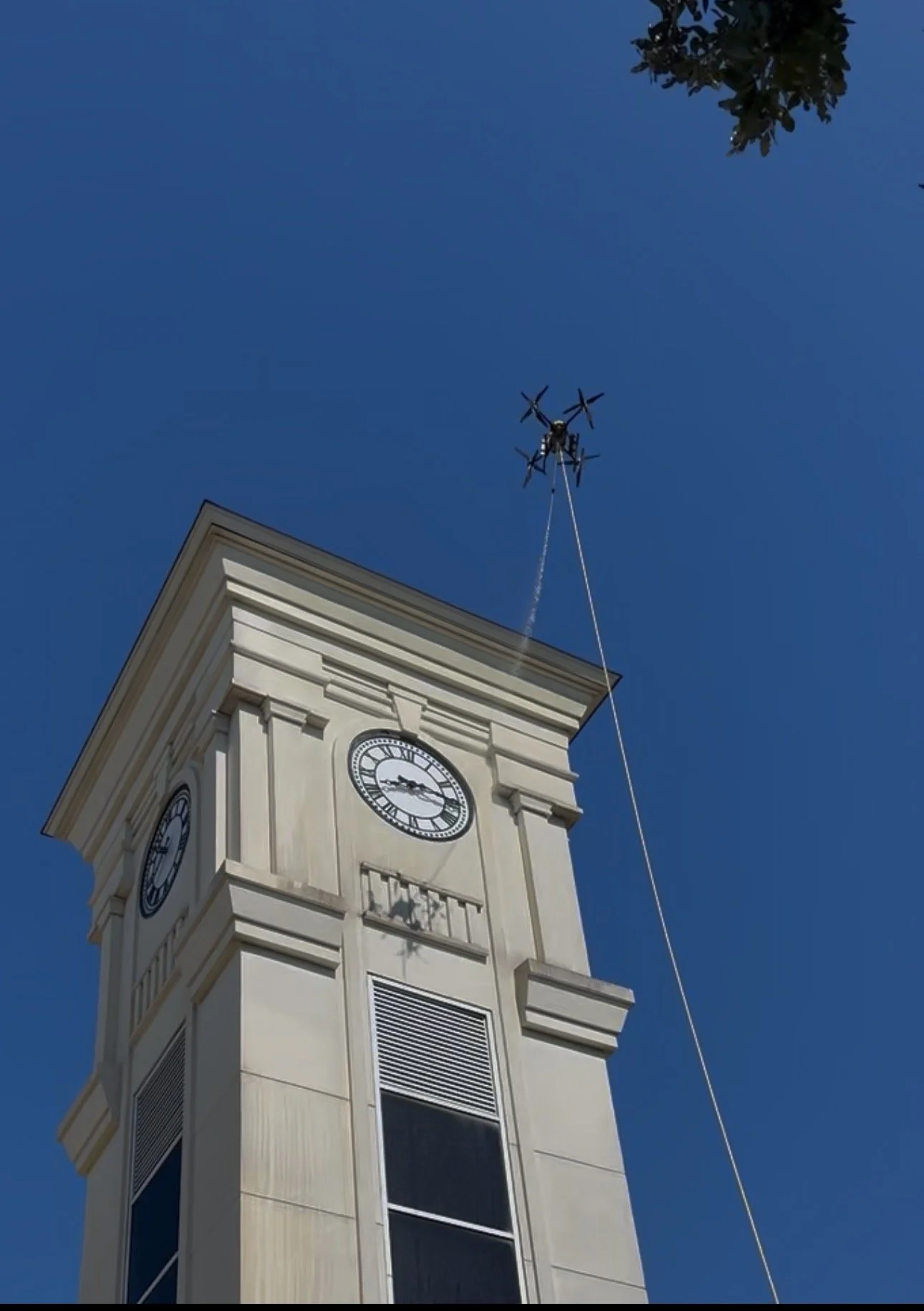 A clock tower with a white facade against a bright blue sky, with a helicopter flying above it.