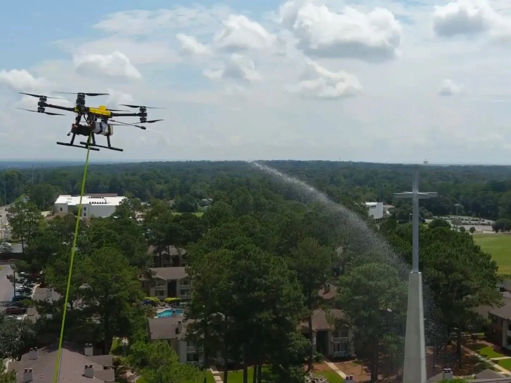 A drone flying over a residential neighborhood, spraying water or chemicals onto the trees and rooftops in the area.