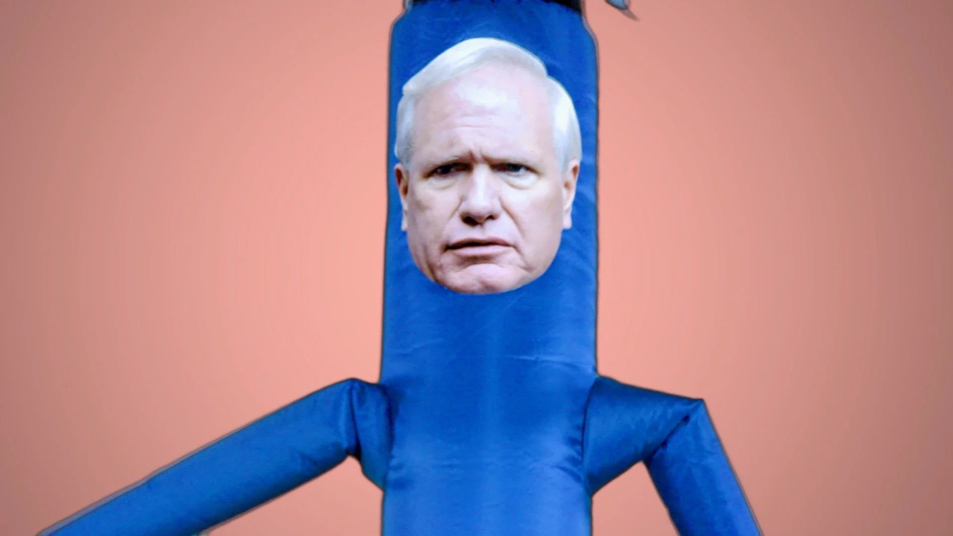 A blue inflatable Air Dancer man with a cutout for a person's face, showing a man with white hair and a serious expression.
