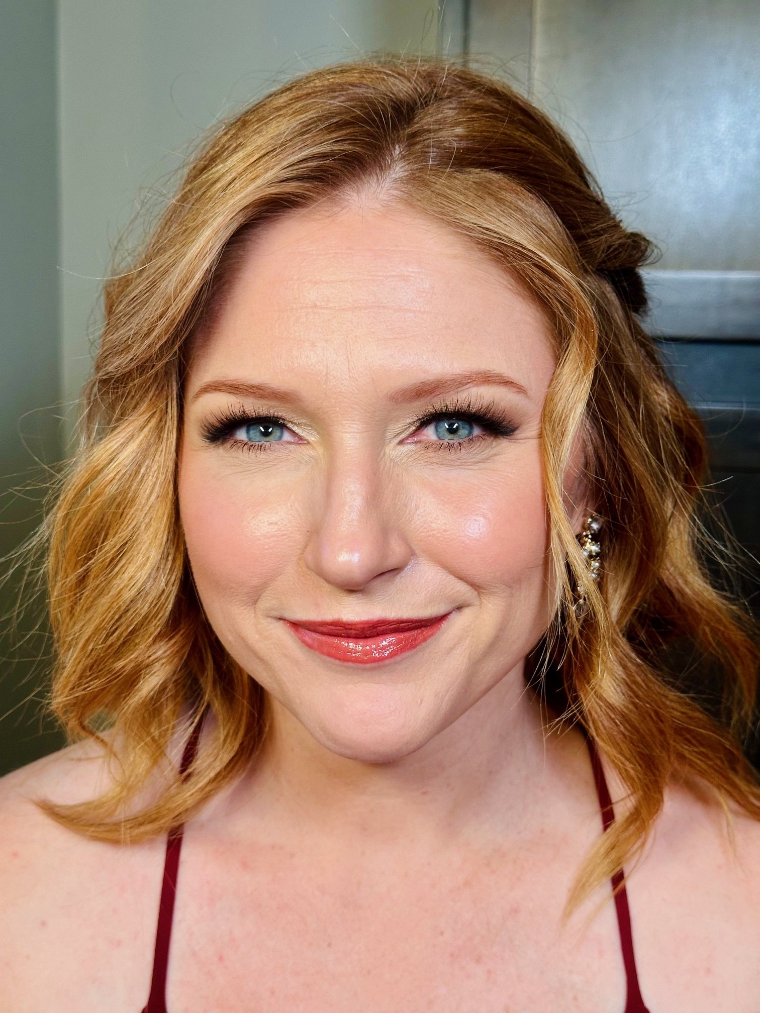 Close-up of a smiling woman with red hair, blue eyes, and red lipstick, wearing a halter top.
