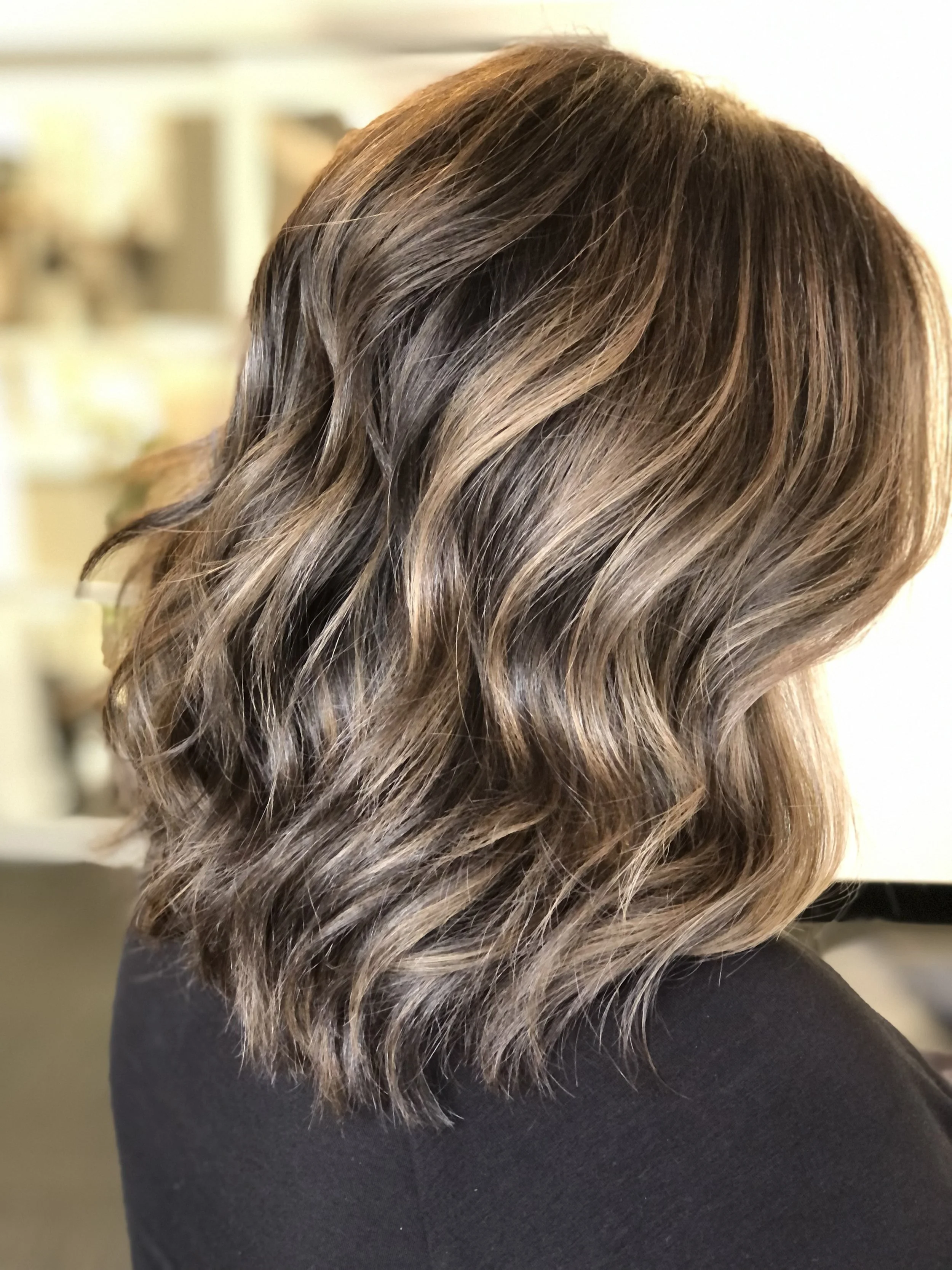 Close-up of styled brown hair with blonde highlights, worn by a person in a black top.
