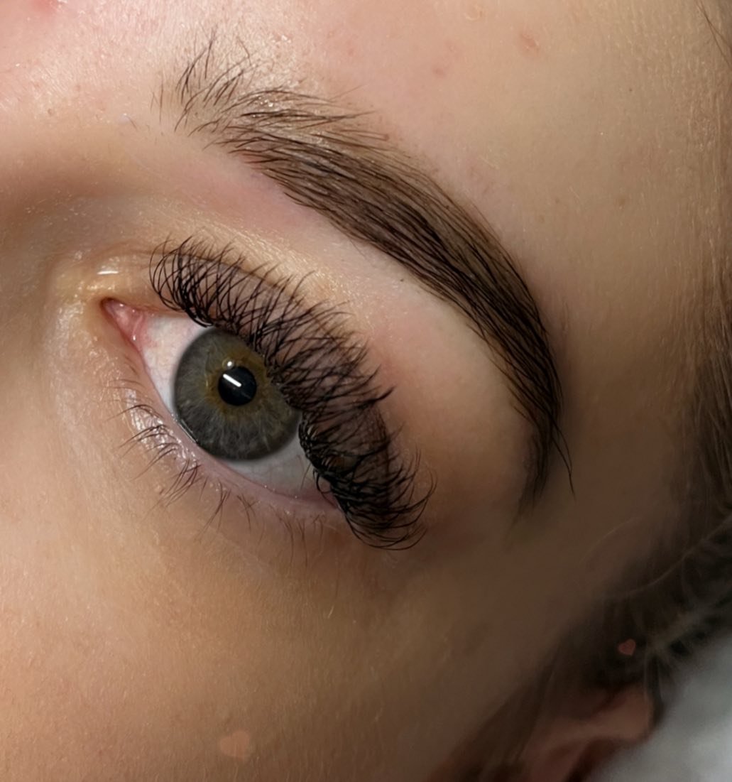 Close-up of a person's eye with natural makeup, focusing on the eyebrow, long eyelashes, and hazel iris.