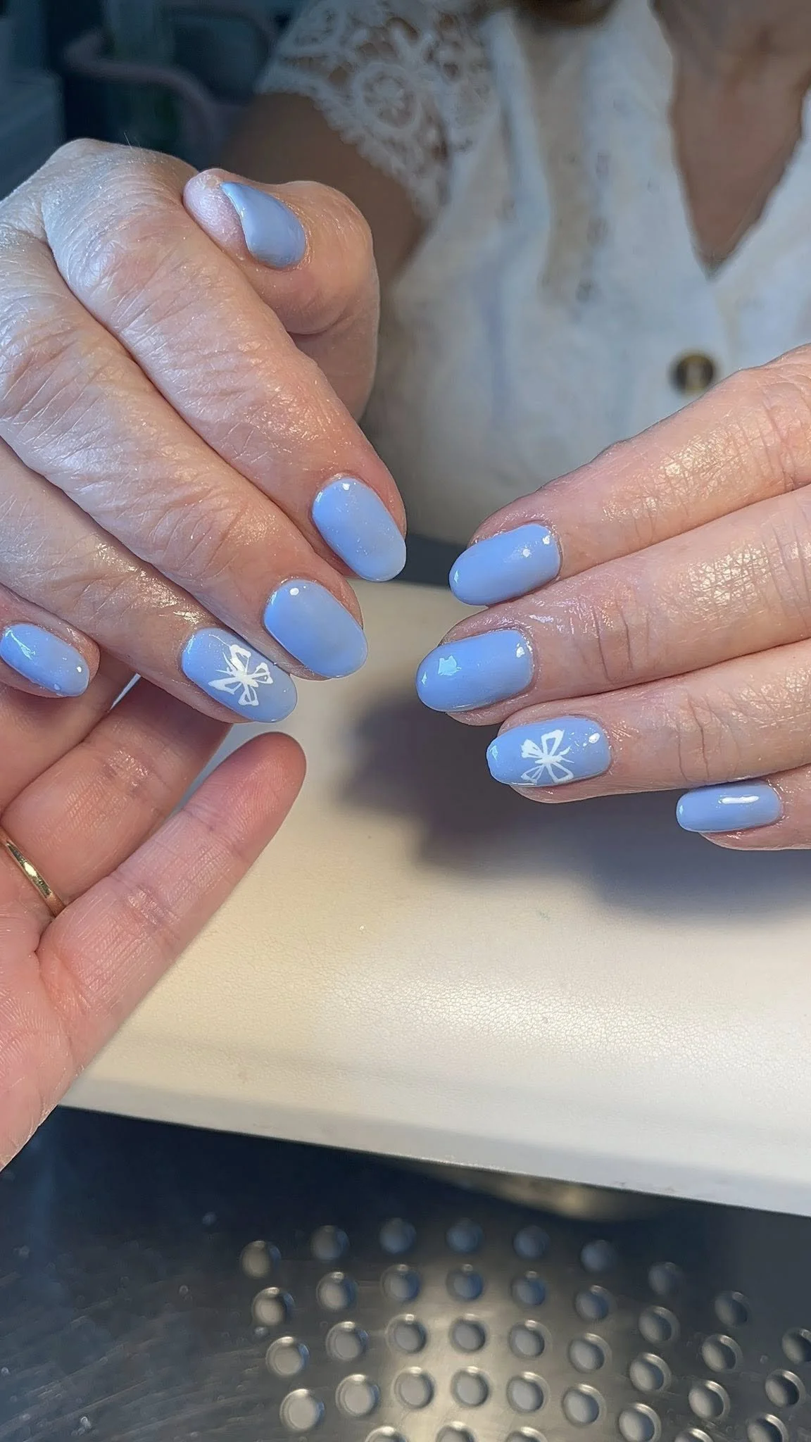 Close-up of a person's manicured nails painted in pastel blue with white snowflake designs on some nails, held over a white surface.