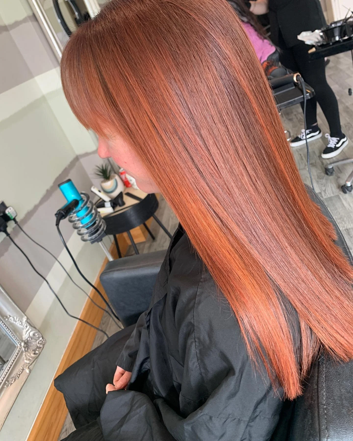 A woman with long, straight, reddish hair sitting in a salon chair, possibly after a hair coloring or styling session.
