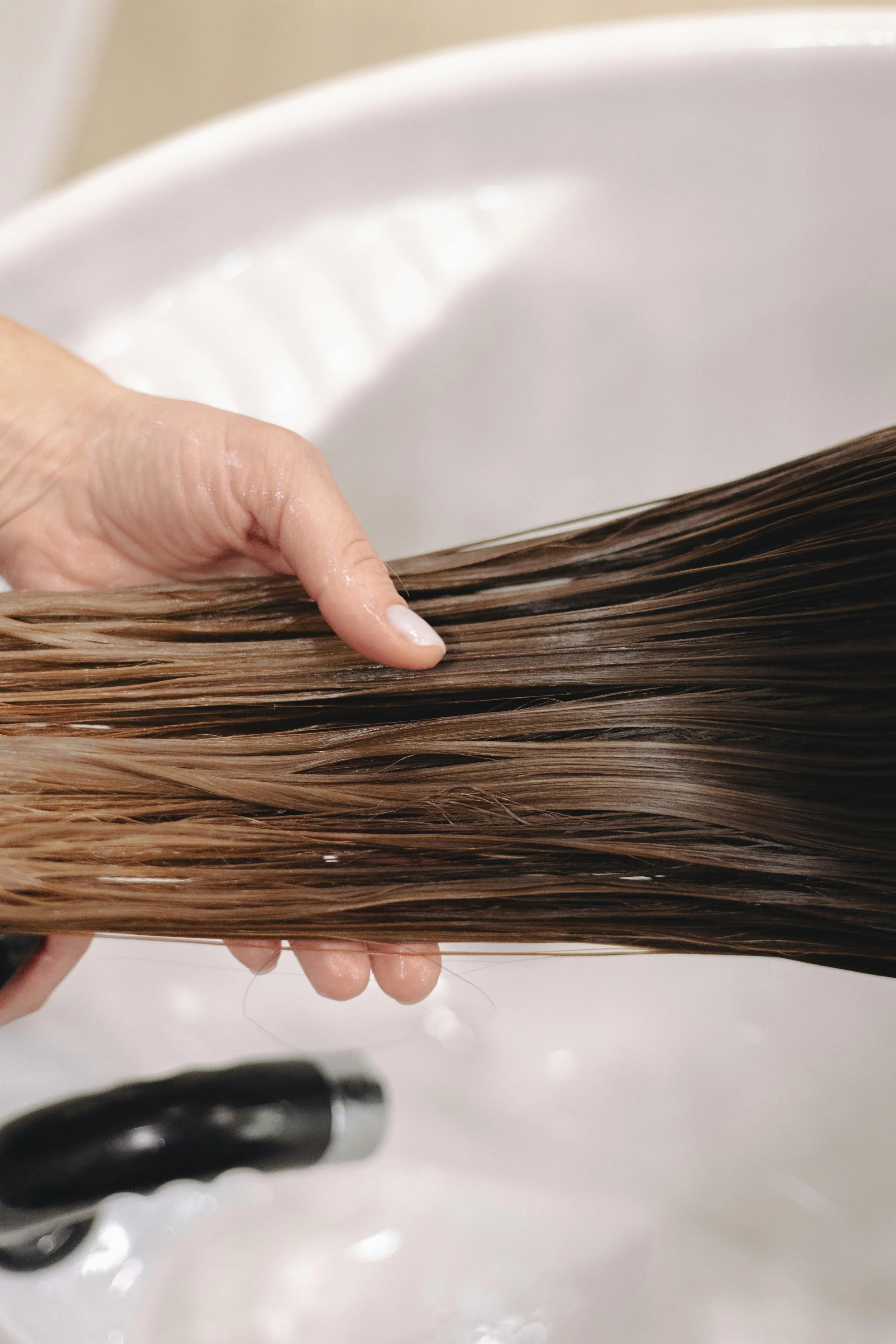 Close-up of a hand holding a bunch of wet brown hair over a sink. A pair of scissors is partially visible at the bottom of the image.
