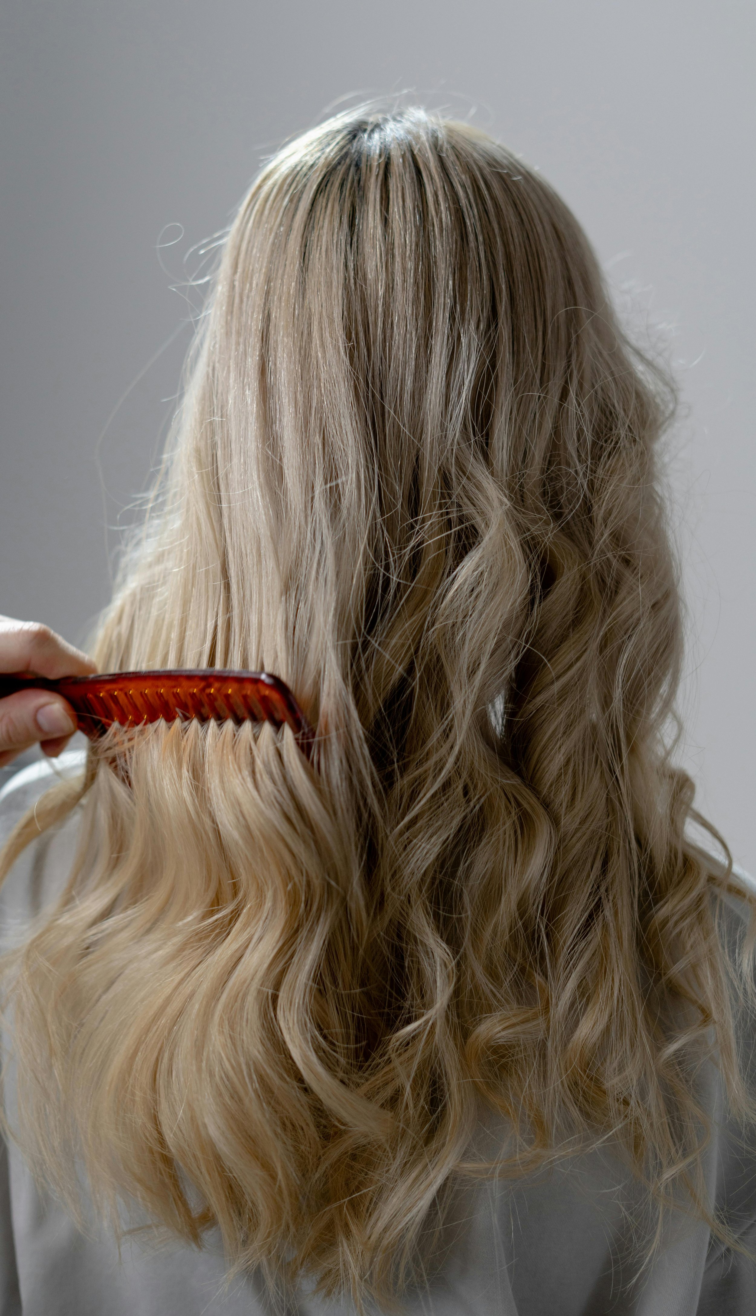 A person with long, blonde, wavy hair is brushing their hair with an orange comb. Lisa B Hair & Beauty Salon, Carlisle, Cumbria UK.