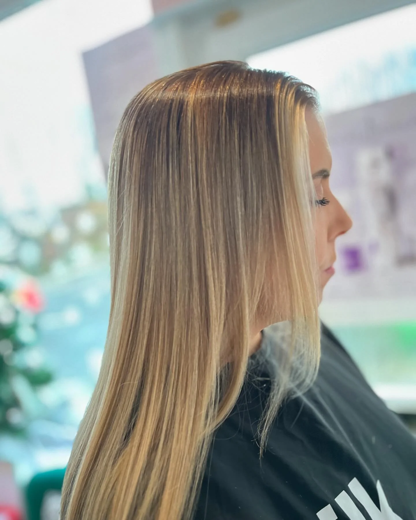 A woman with long, straight blonde hair and light skin, sitting with her eyes closed in a salon or similar setting.
