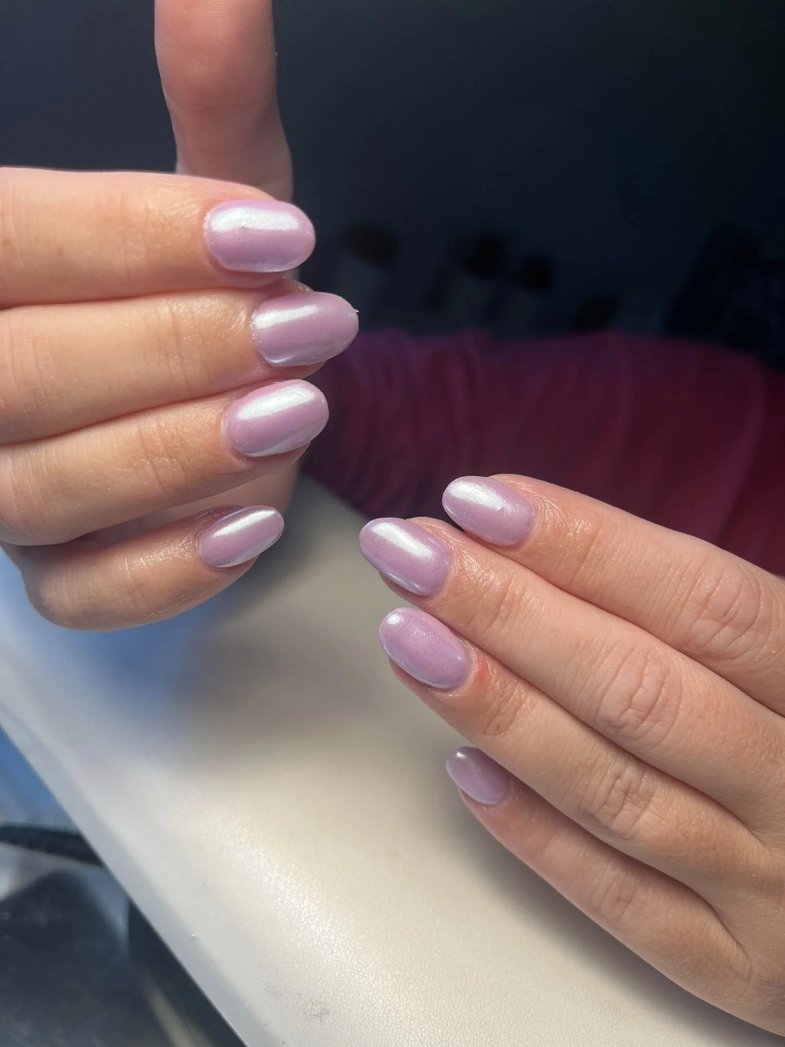 Close-up of hands with manicured nails painted with shiny, pearly pink nail polish.
