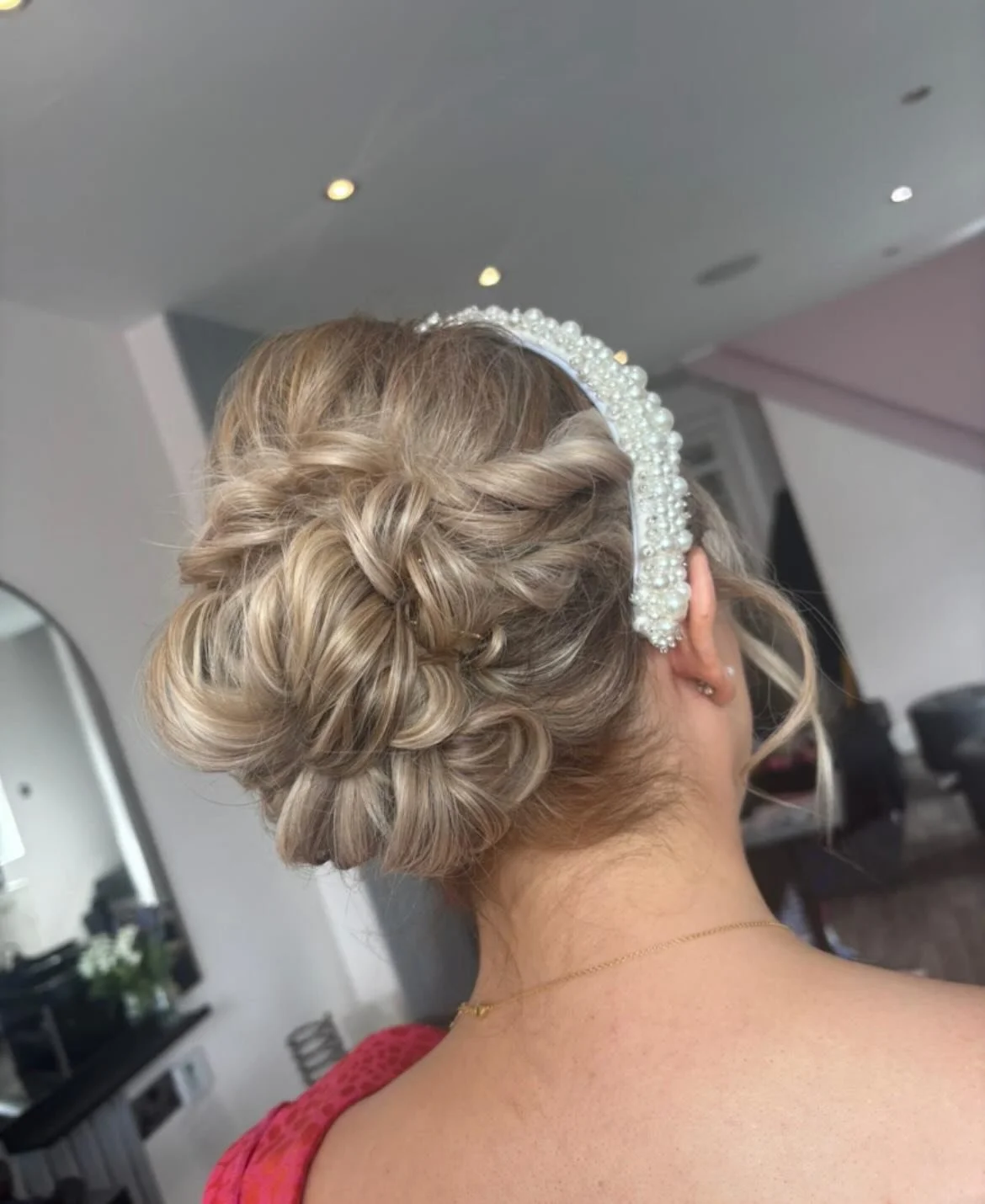 A woman with blonde hair styled in an intricate updo with multiple twists and braids, wearing a pearl and bead embellished headband.