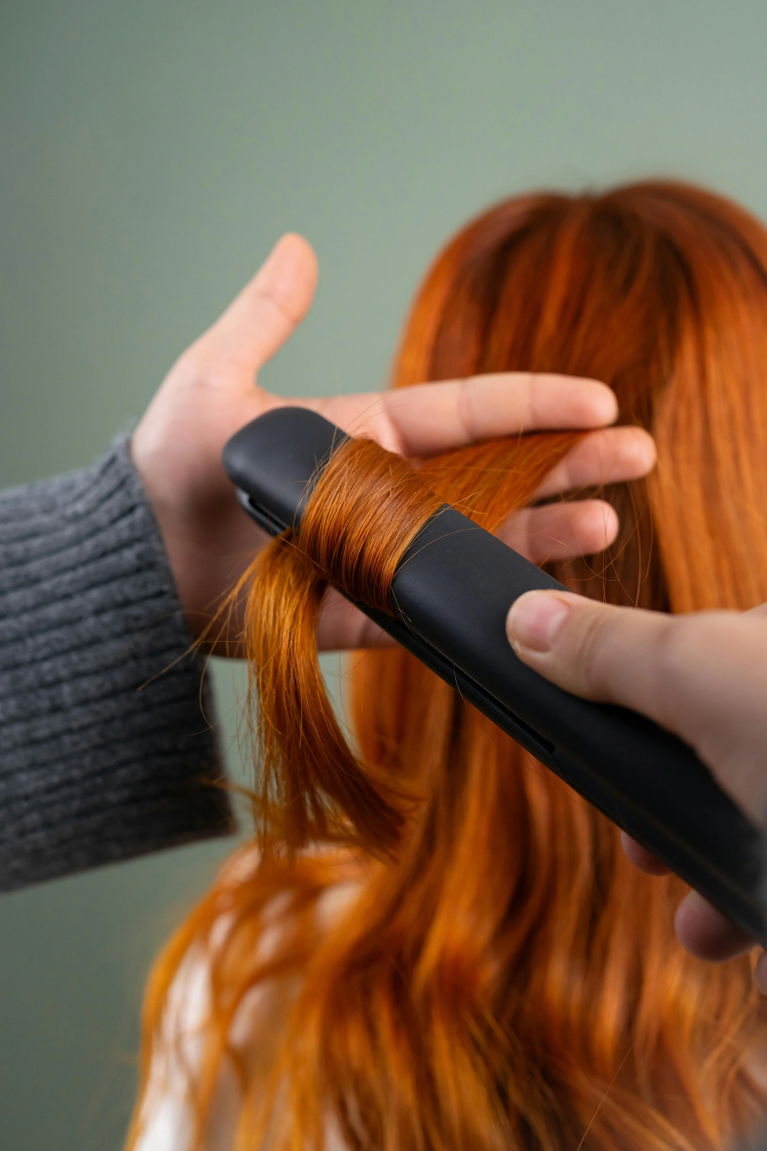 Hairdresser curling a section of long, red hair with a curling iron.