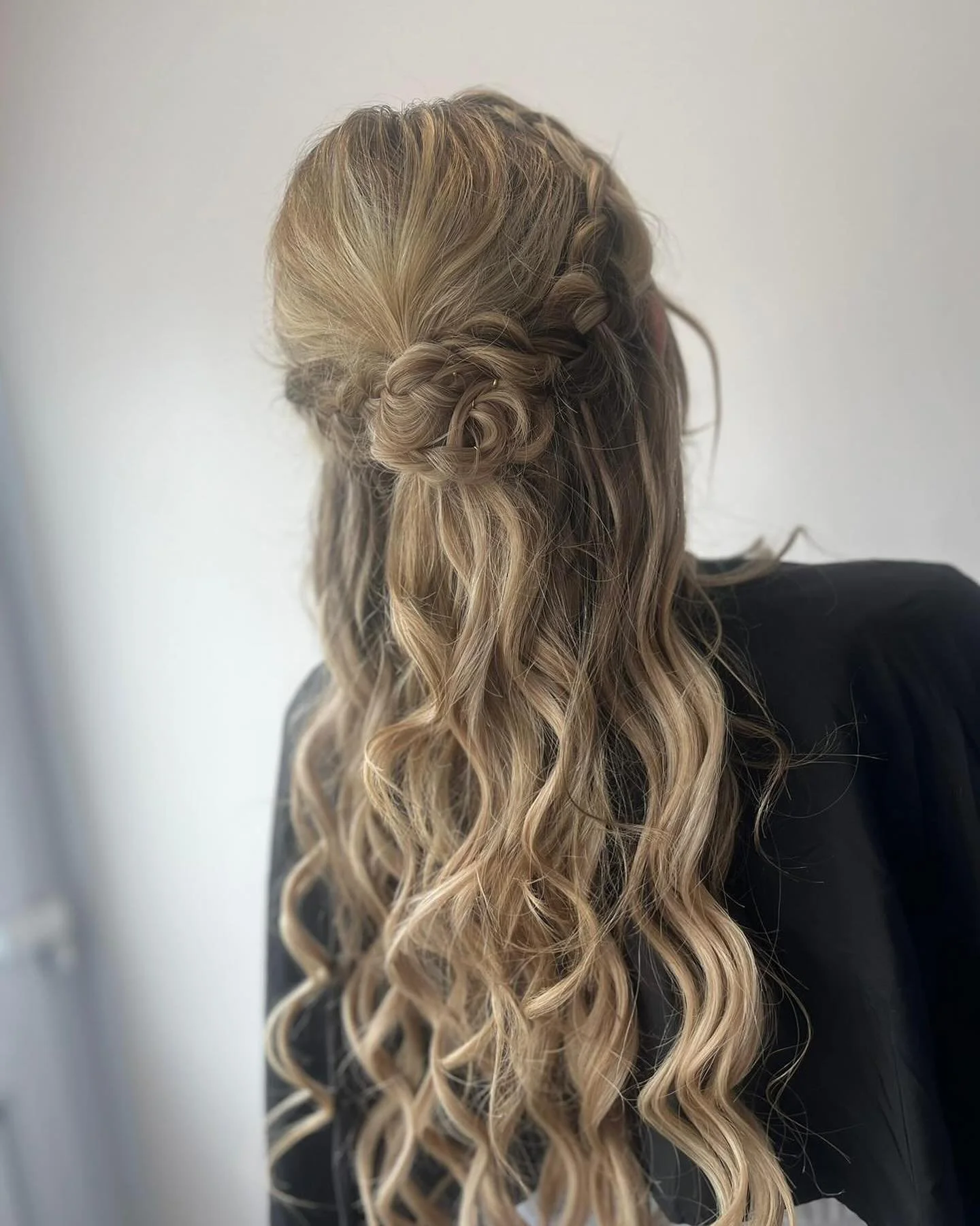 Back view of a woman with long, blonde, curly hair styled in a half-up hairstyle with twisted sections.
