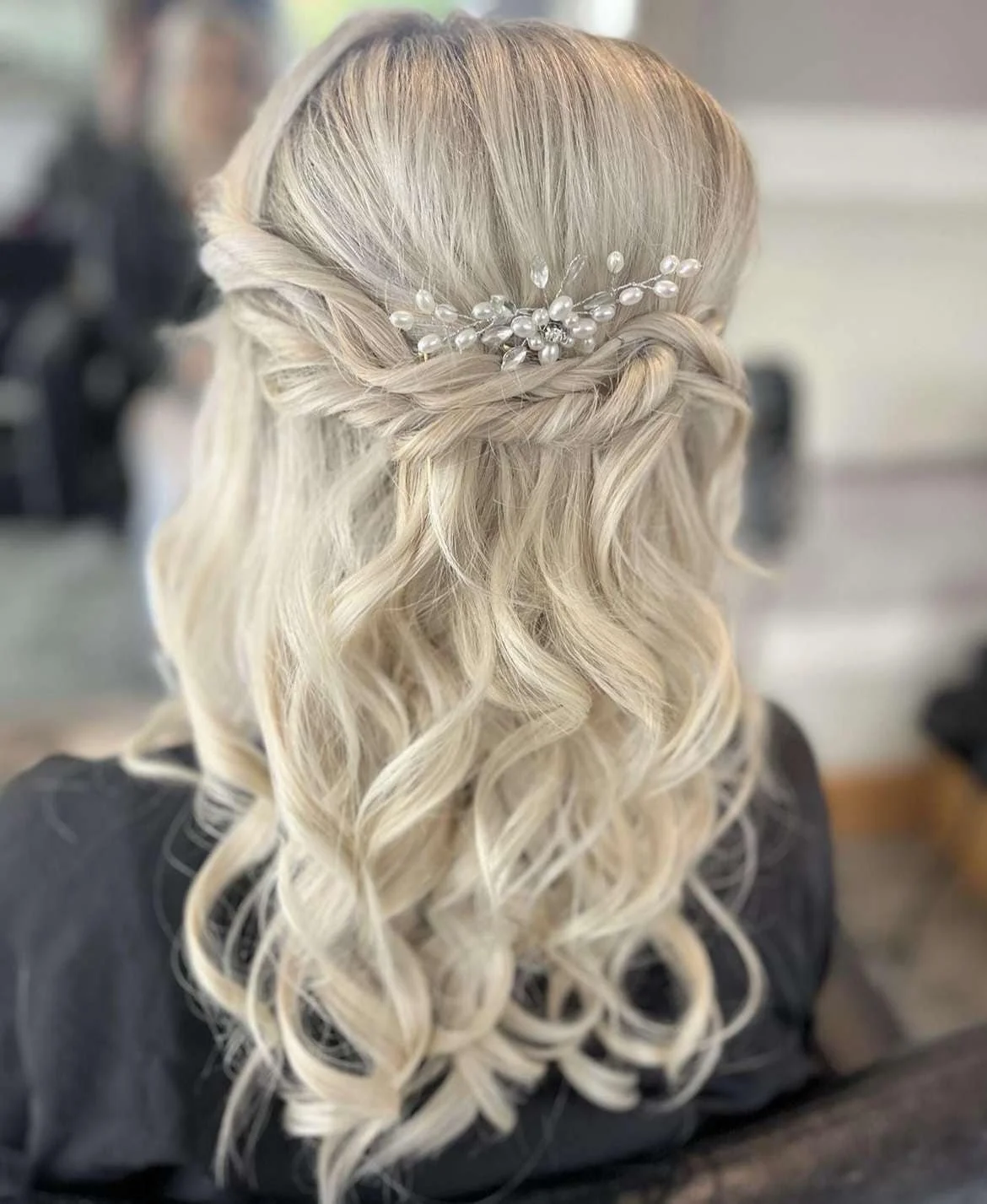 A woman with long, wavy platinum blonde hair styled in soft curls, decorated with a pearl and crystal hairpiece.