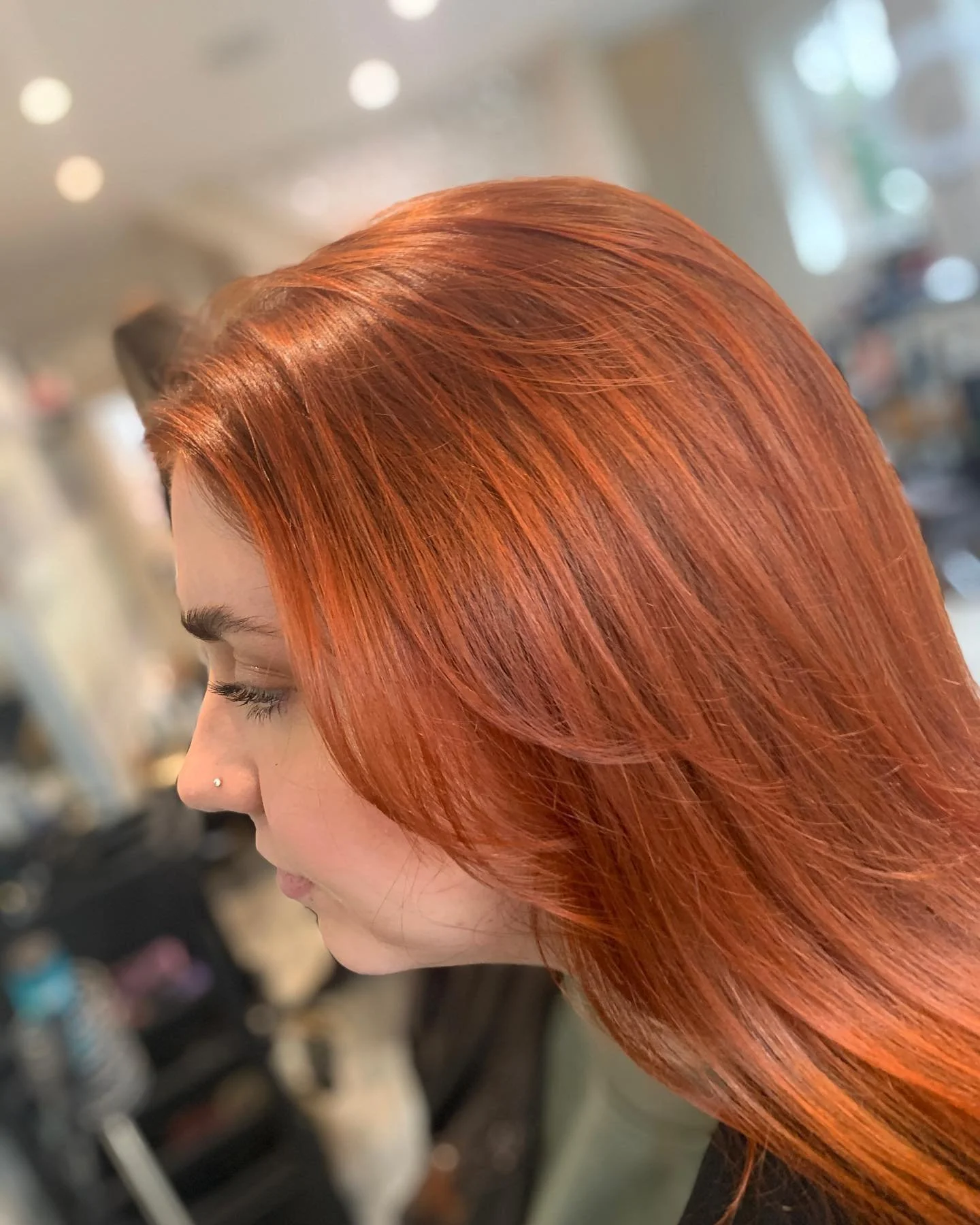Close-up side profile of a woman with vibrant red hair in a sleek, shiny style, with a blurred background.