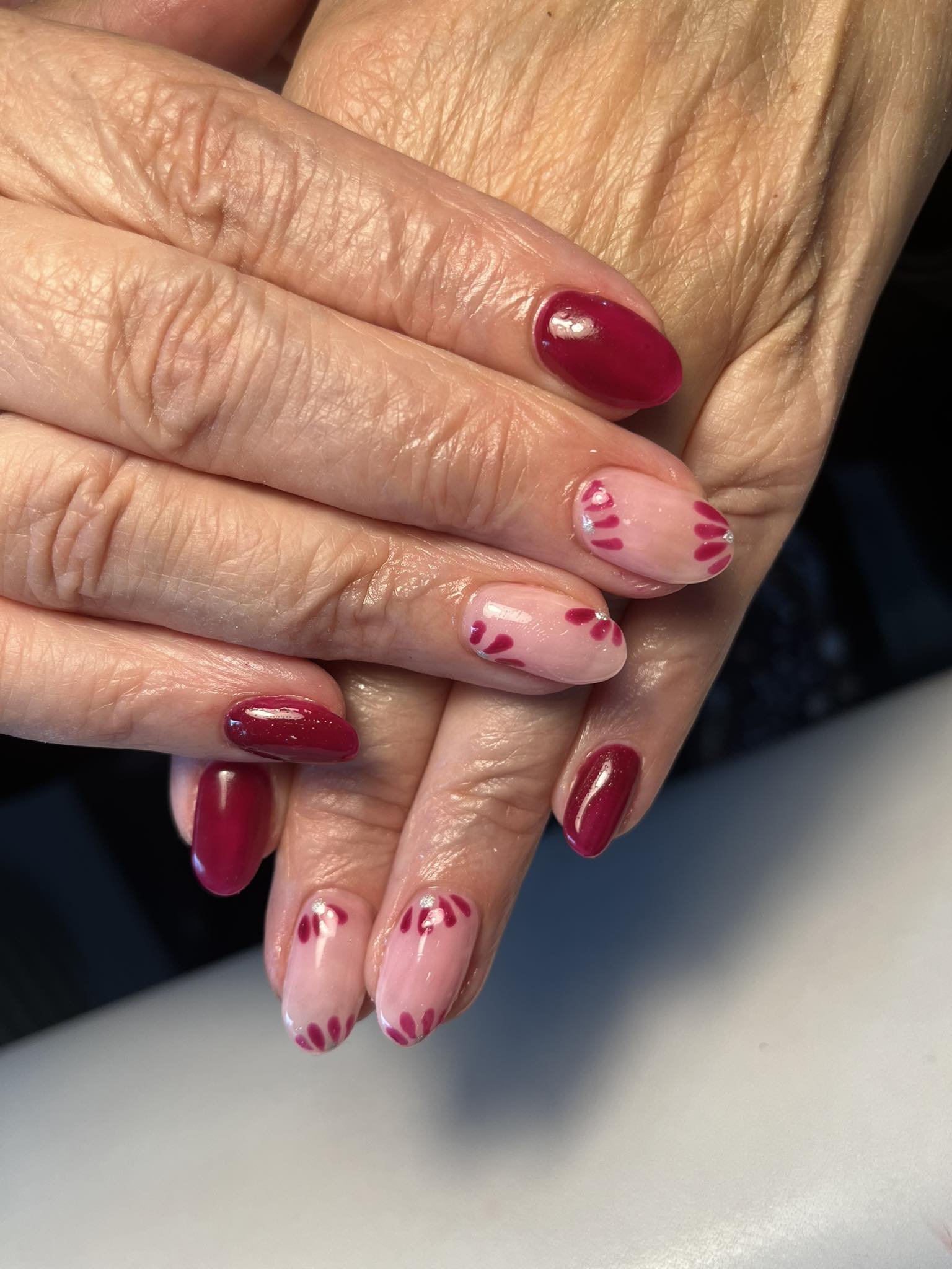 Close-up of a hand with pink and red manicured nails, featuring heart and stripe designs on some nails.