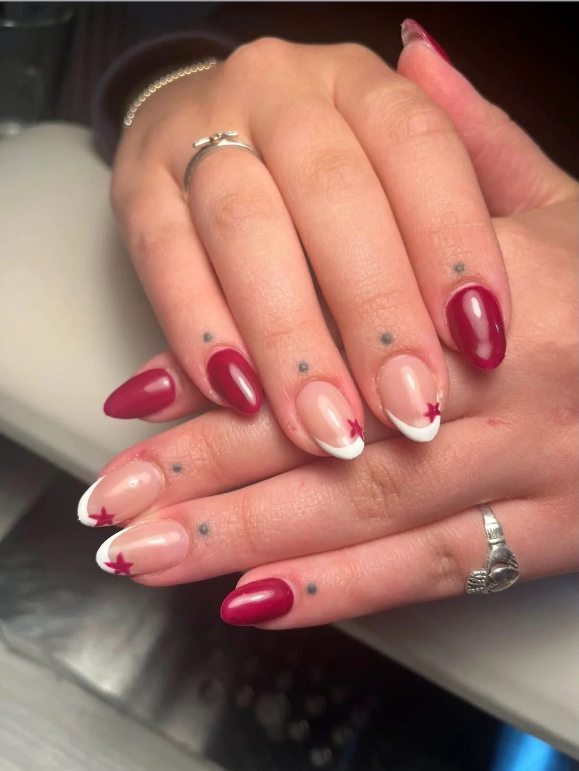 Close-up of manicured hands with red, white, and clear nails with red stars, small tattoos, and rings. Award winning Lisa B Hair and Beauty Salon in Carlisle, Cumbria UK.