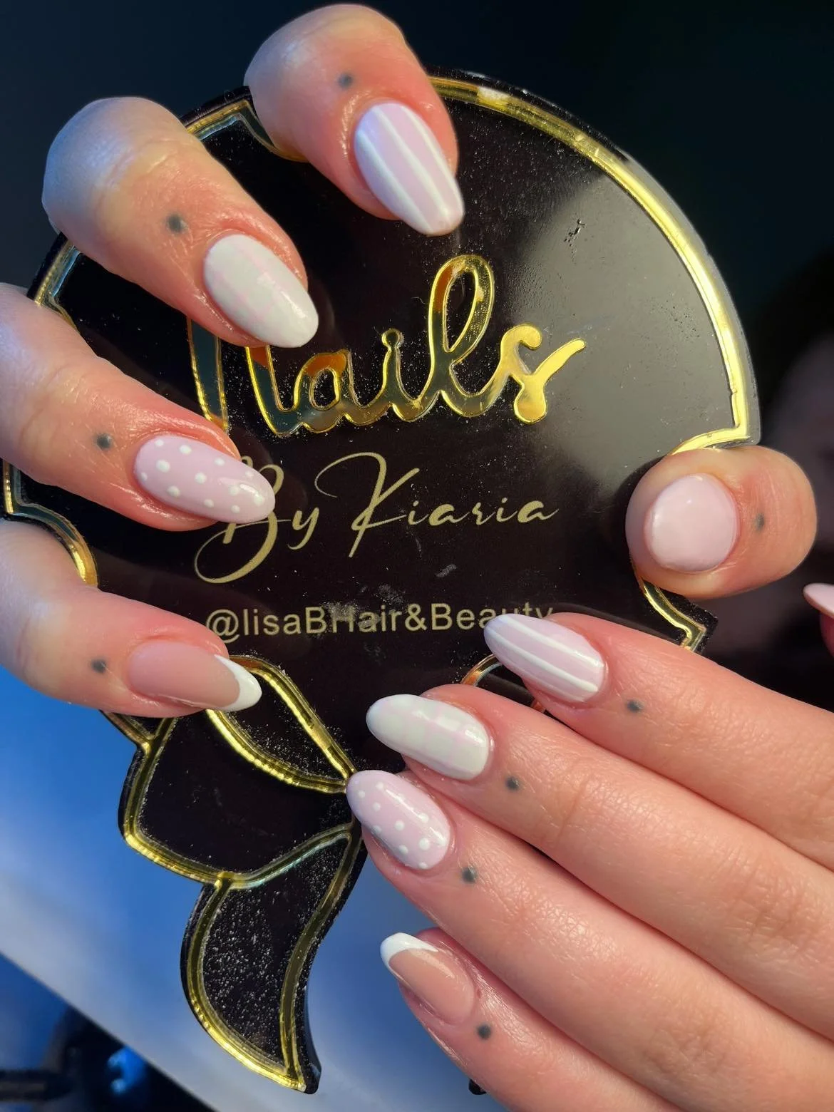 Close-up of hands with manicured nails holding a black and gold sign that says "Lails by Kiaria" and the Instagram handle "@lisaBHair&Beauty".