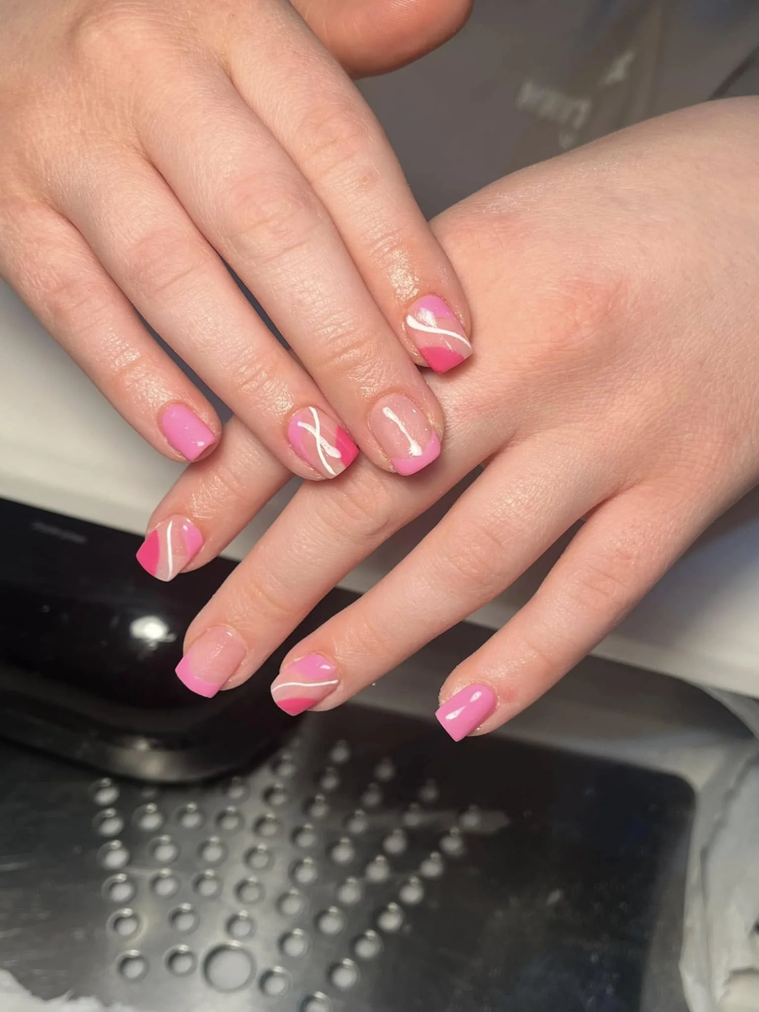 Close-up of hands with pink and white French manicured nails with swirl designs on a metallic surface. Award winning Lisa B Hair and Beauty Salon in Carlisle, Cumbria UK.