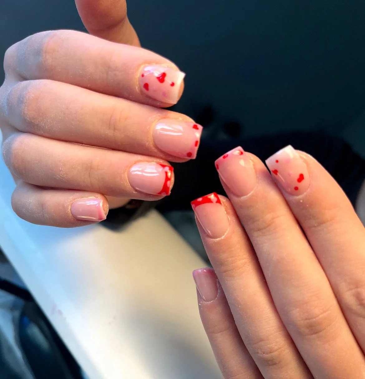Close-up of a person's hands with clear nails and red splatter nail art, resembling blood spatters. Award winning Lisa B Hair and Beauty Salon in Carlisle, Cumbria UK.