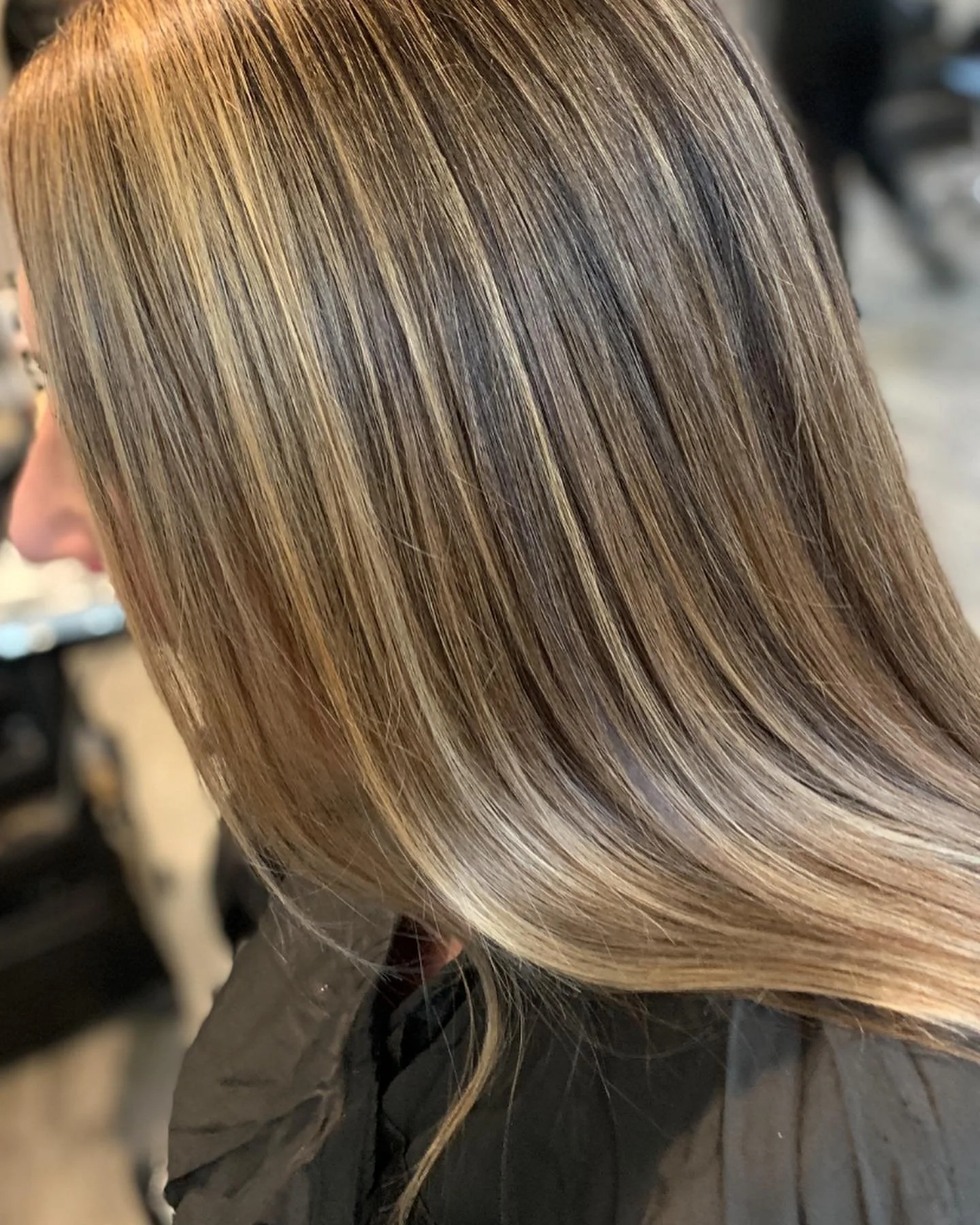 Close-up of a person with straight, blonde hair with lowlights, sitting in a salon chair wearing a black cape.