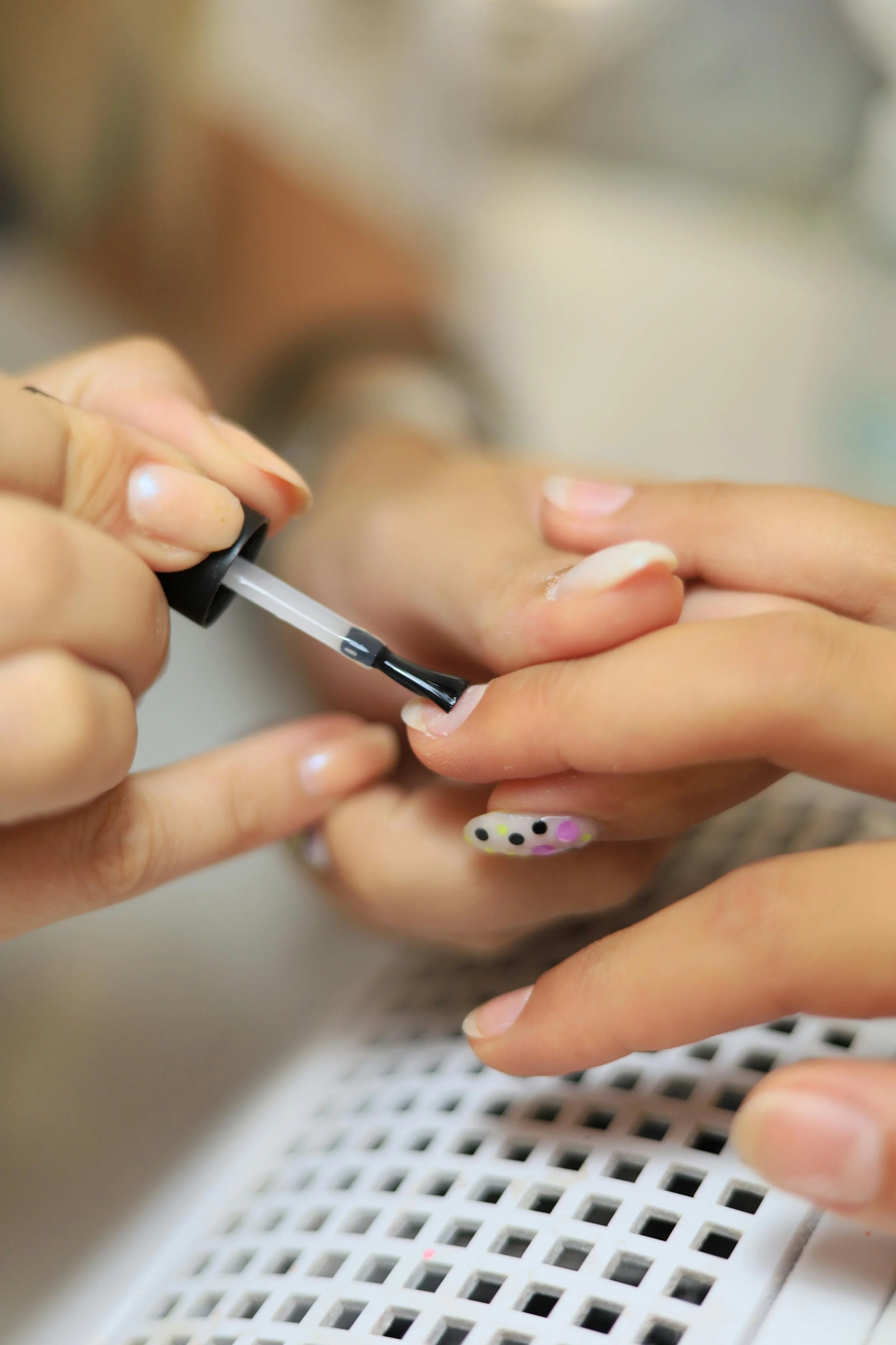 Close-up of hands applying clear nail polish to fingernails, with a nail polish brush in focus and a patterned nail on one finger.
