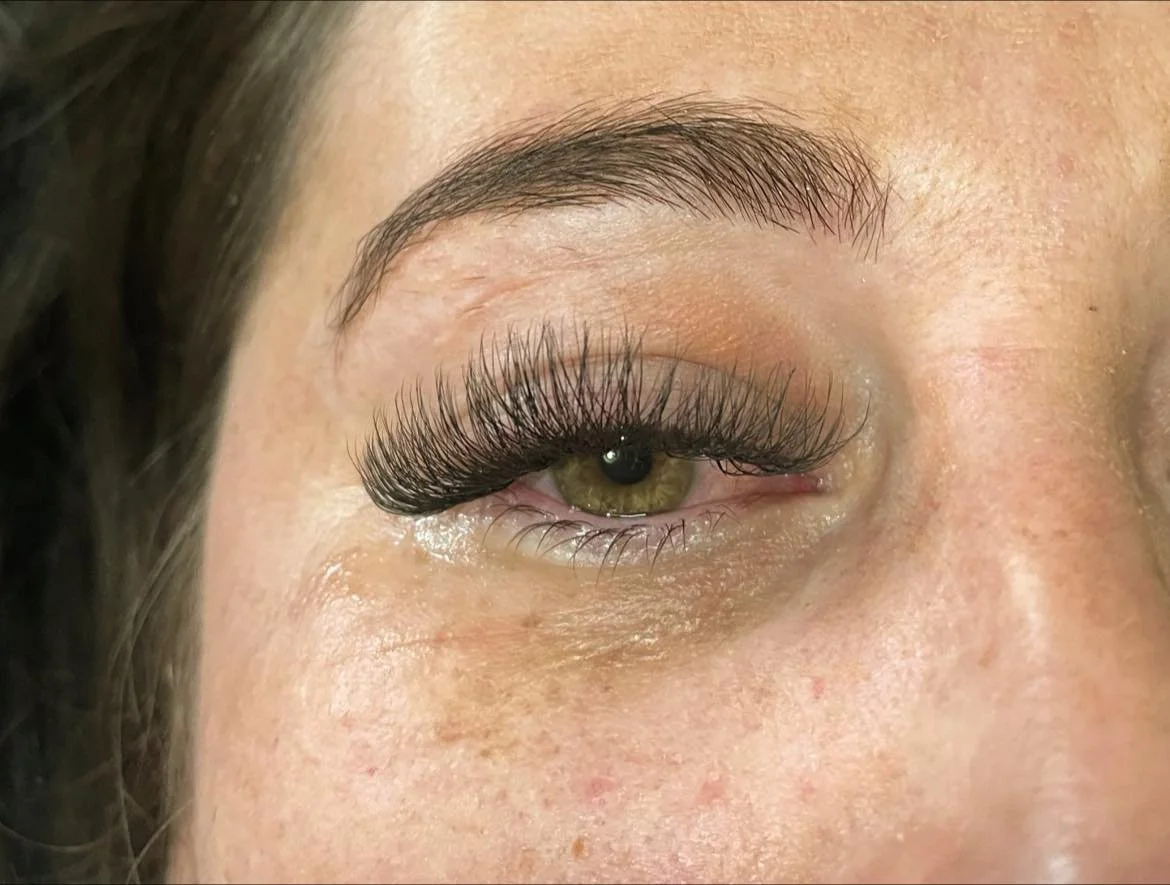Close-up of a woman's eye with long false eyelashes, light makeup, and a visible eyebrow.