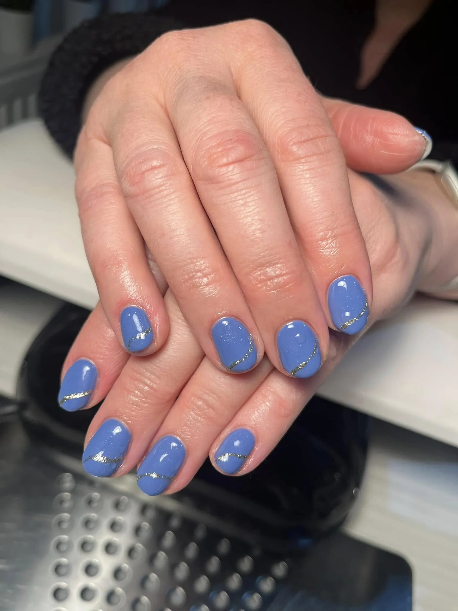 Close-up of hands with blue painted nails featuring silver glitter wavy lines and a shiny finish. Award winning Lisa B Hair and Beauty Salon in Carlisle, Cumbria UK.