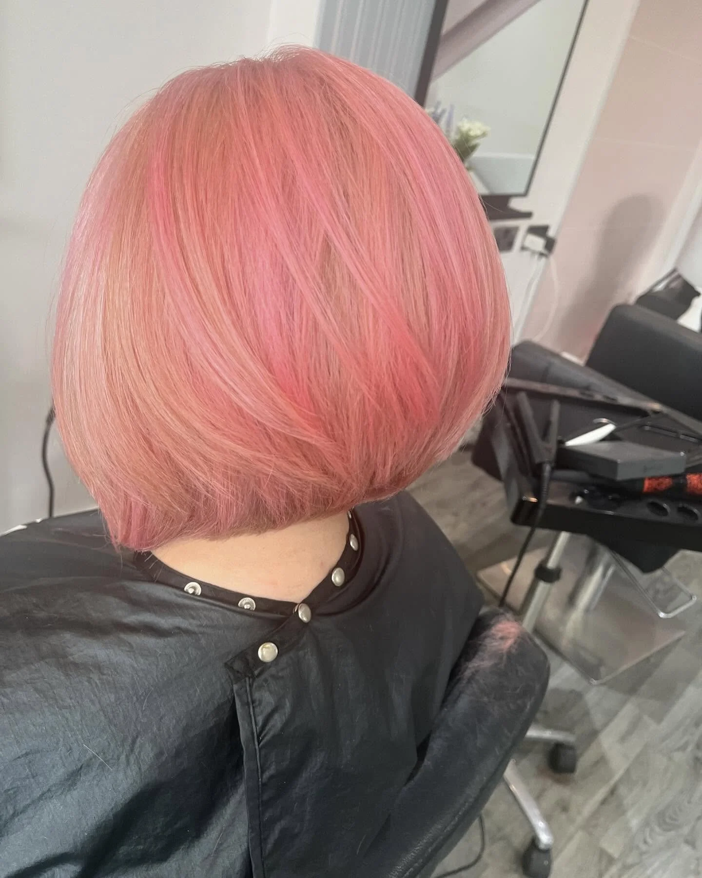 Person with short, layered pink hair sitting in a salon chair, facing away, with salon equipment visible in the background.