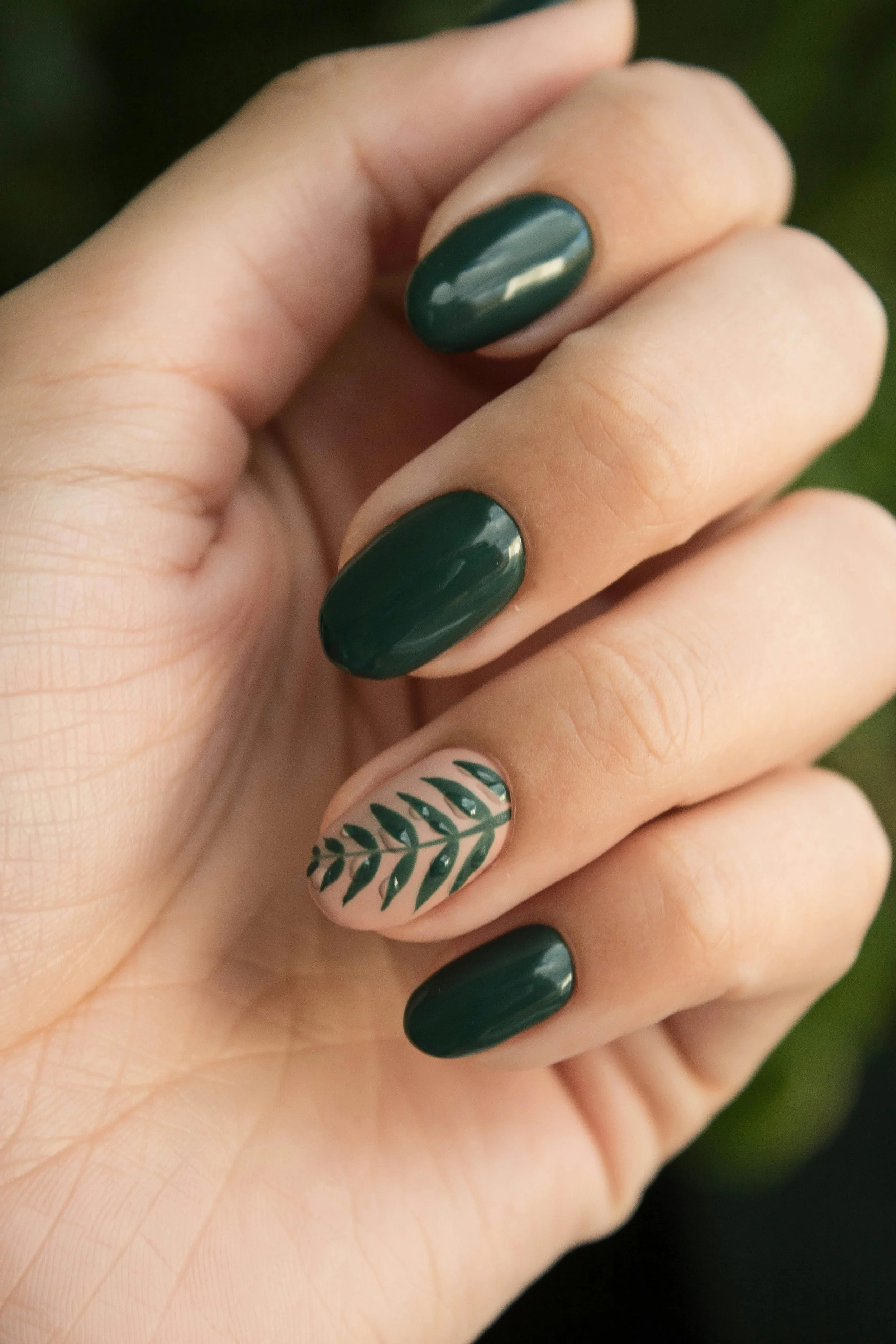 Close-up of a hand with dark green painted nails and one nail decorated with a green leaf pattern. Award winning Lisa B Hair and Beauty Salon in Carlisle, Cumbria UK.