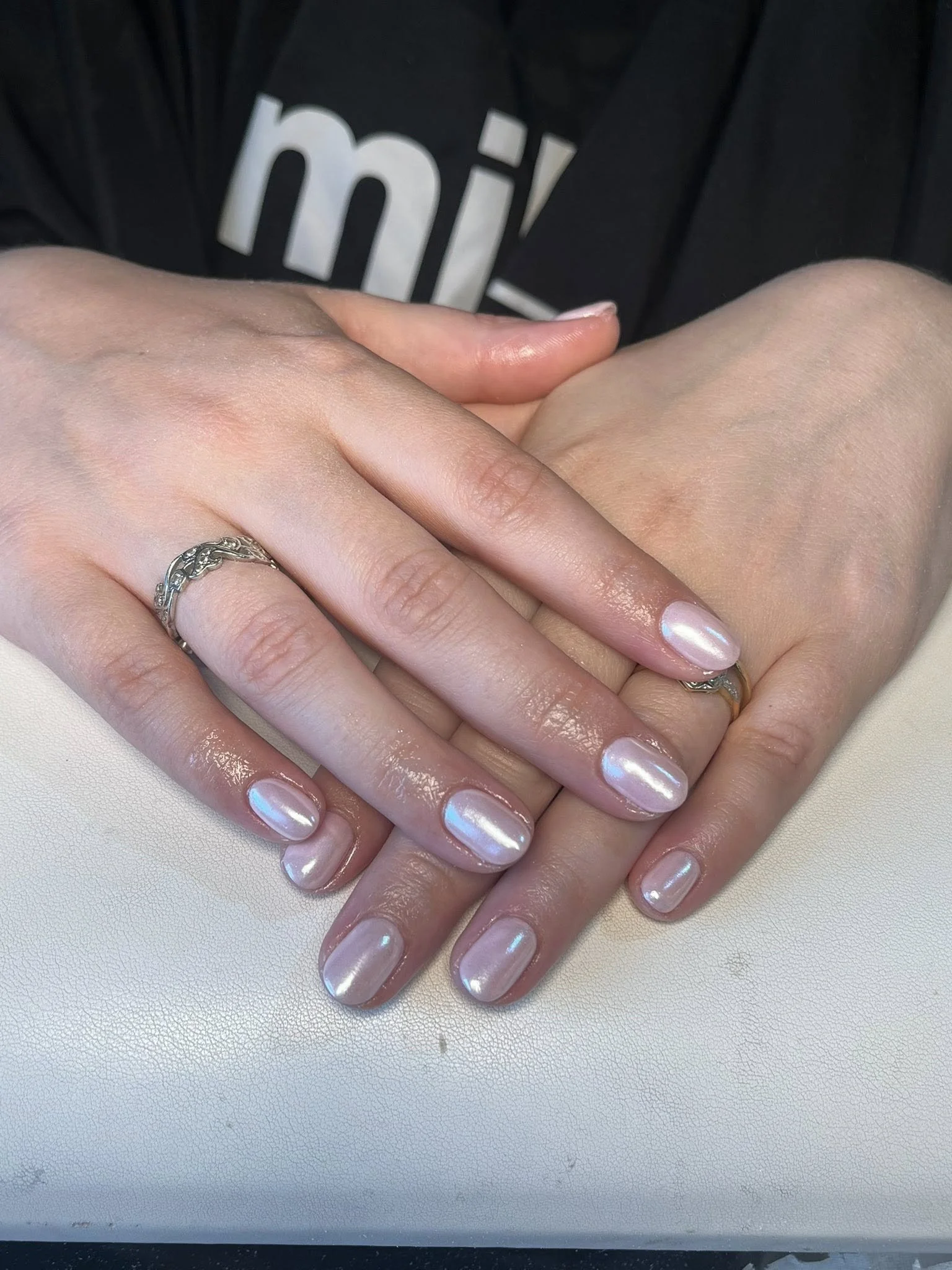 Close-up of hands with manicured nails and rings, resting on a white surface.