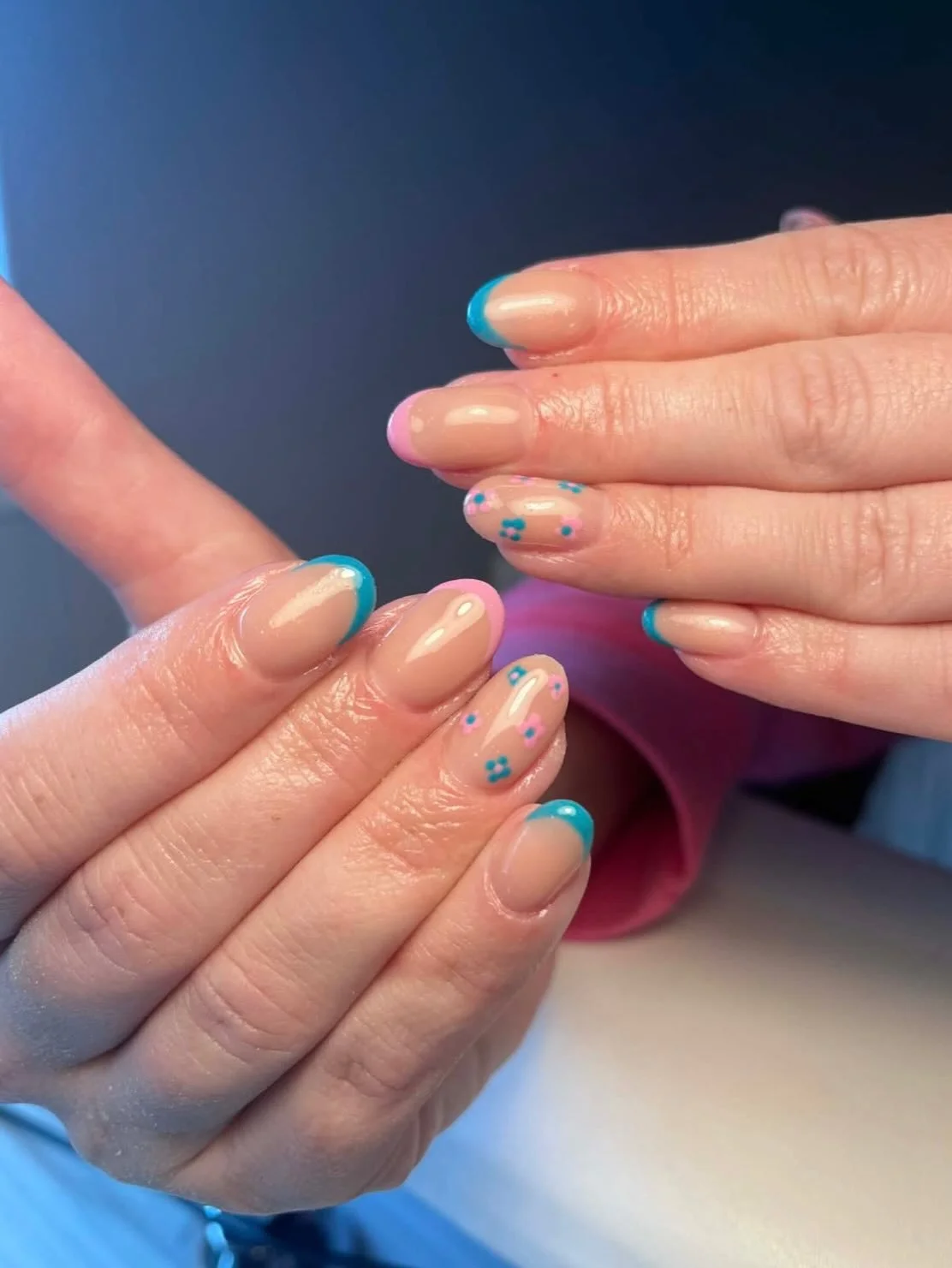 Close-up of hands with manicured nails featuring beige polish with blue and pink flower and tip accents. Award winning Lisa B Hair and Beauty Salon in Carlisle, Cumbria UK.