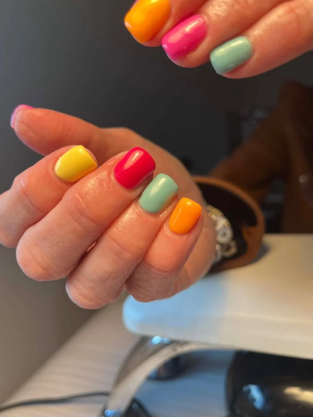 Close-up of a hand with colorful nail polish on all fingernails, including yellow, red, mint green, and orange colours. Award winning Lisa B Hair and Beauty Salon in Carlisle, Cumbria UK.