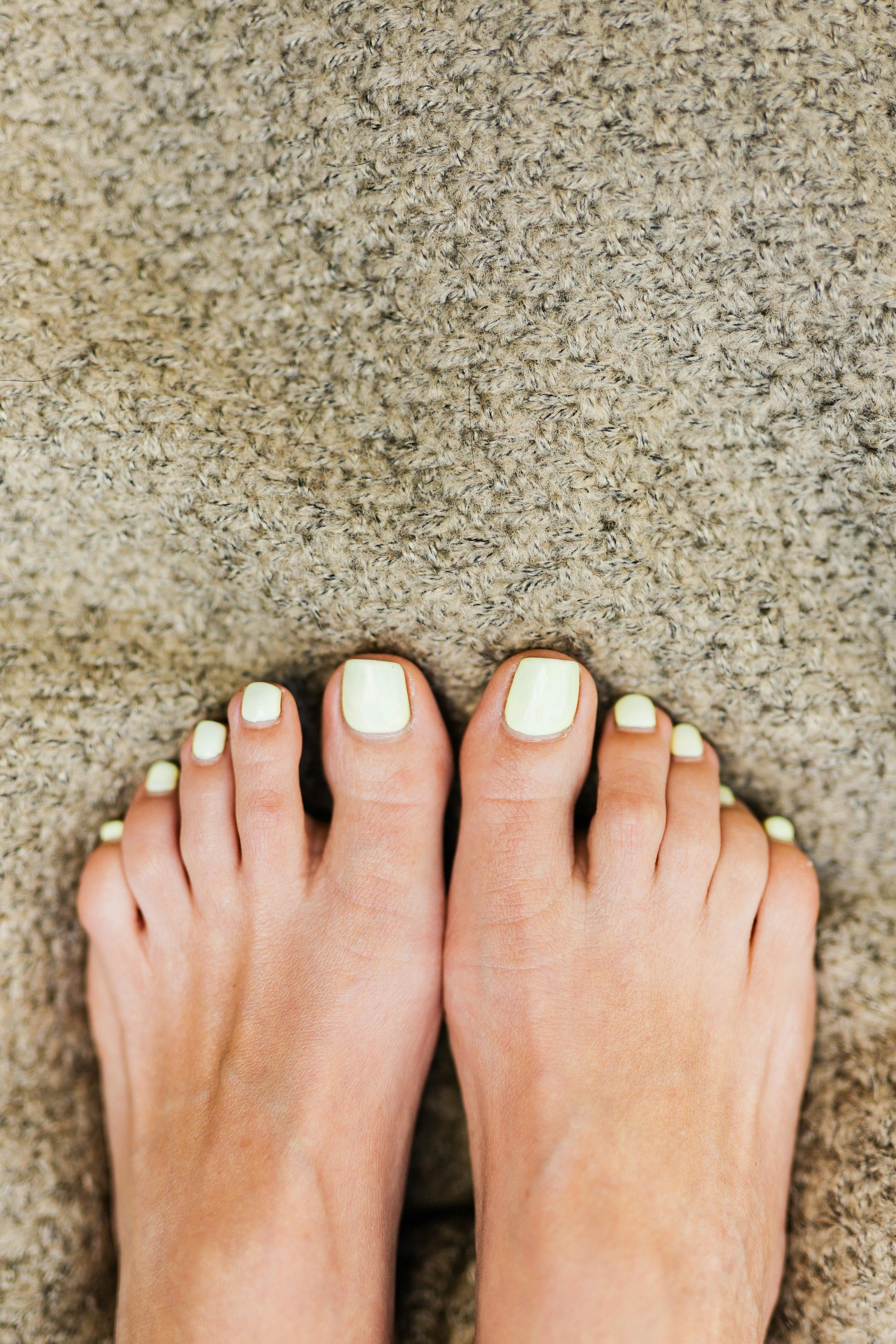 Two hands with yellow painted nails resting on a textured grey carpet. Award winning Lisa B Hair and Beauty Salon in Carlisle, Cumbria UK.