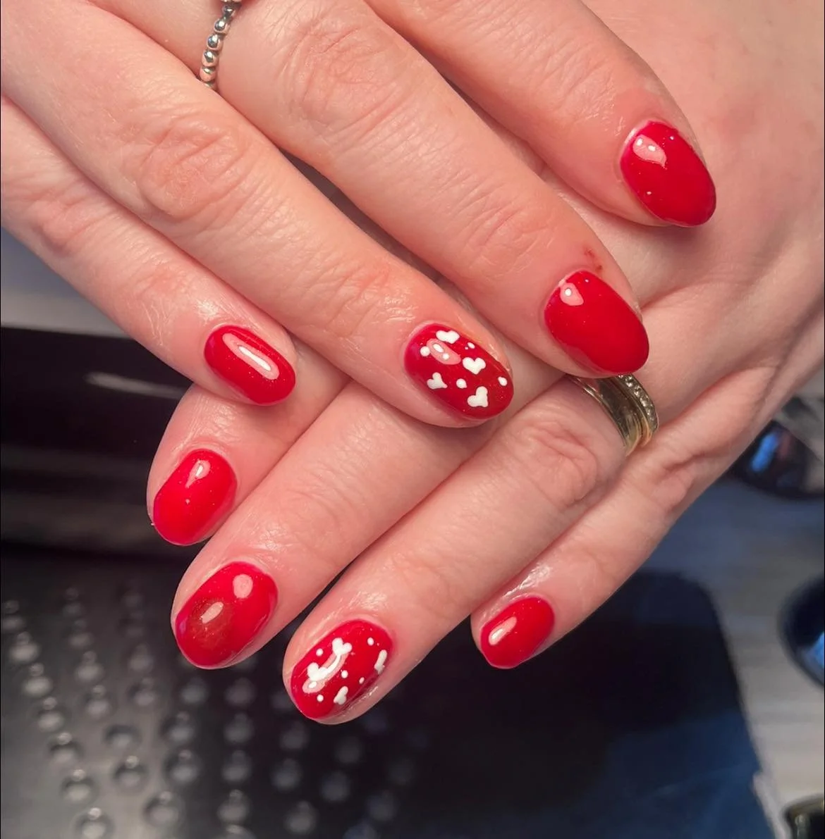 Close-up of manicured nails painted red with white heart and snowflake designs, with hands overlapping. Award winning Lisa B Hair and Beauty Salon in Carlisle, Cumbria UK.