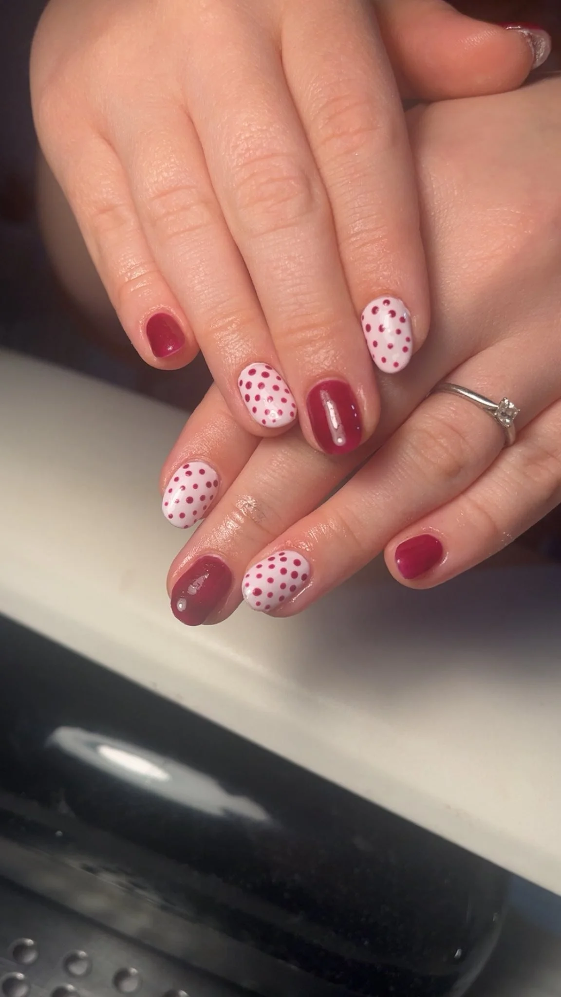 Close-up of a person's hands with manicured nails, featuring alternating red and white nails with red polka dots at Award winning Lisa B Hair and Beauty Salon in Carlisle, Cumbria UK.