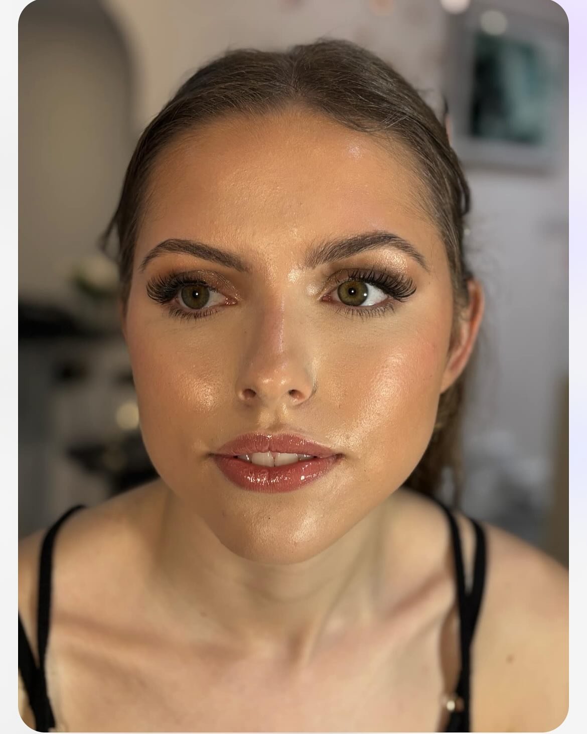 A close-up of a young woman with long brown hair, wearing makeup including eye shadow, mascara, and lipstick, looking slightly to the side.