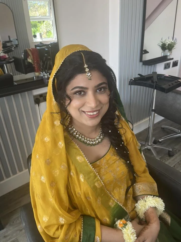 A woman dressed in traditional yellow and green Indian attire sitting in a room with a smile at Lisa B Hair & Beauty Salon, Carlisle, Cumbria UK.