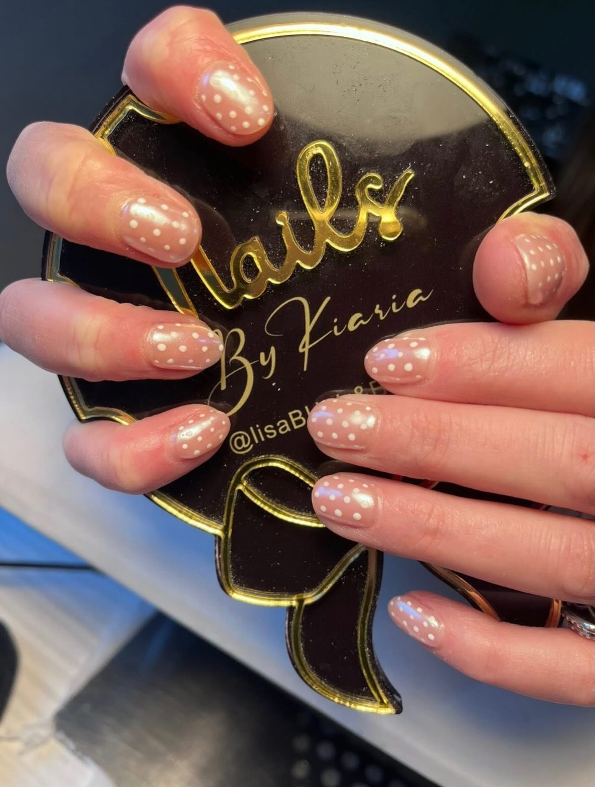 Nails painted with a clear polish and white polka dots, holding a black and gold makeup compact labeled 'Lalis by Kiara' with an Instagram handle '@lisaBh' visible.