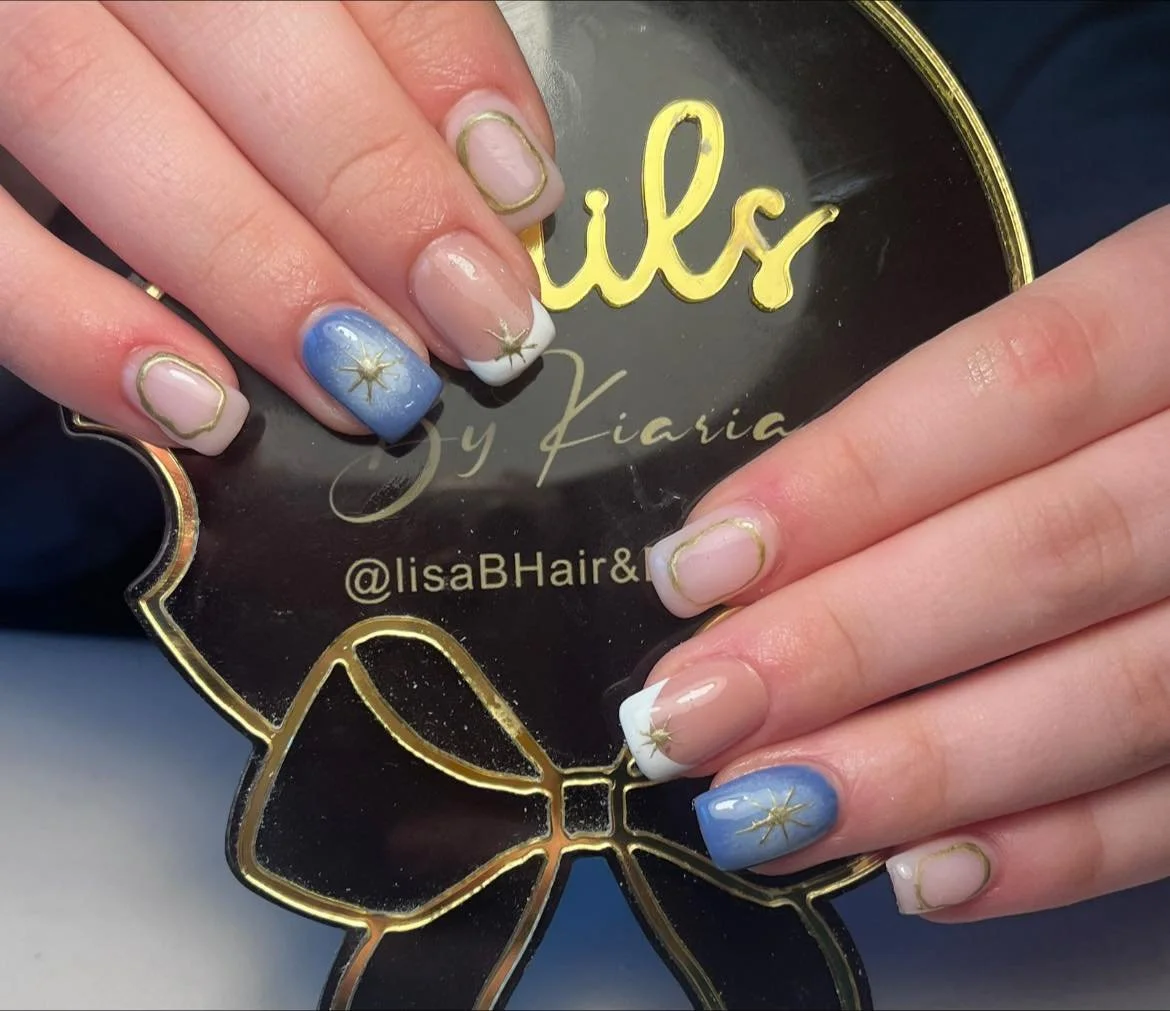 Nail art with pink, white, and blue polish featuring gold starburst designs and gold outline frames on a black and gold sign with the words 'Luxe by Kiara' and '@lisaBHair&'.