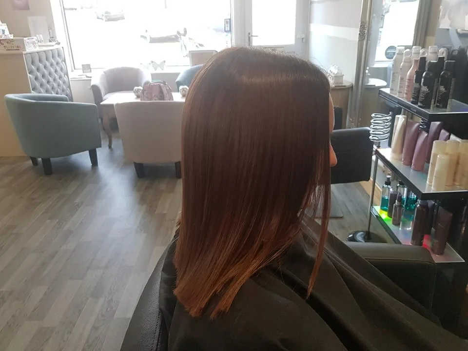 Woman with shiny straight brown hair sitting in a salon with shelves of hair products nearby and chairs around in the background.