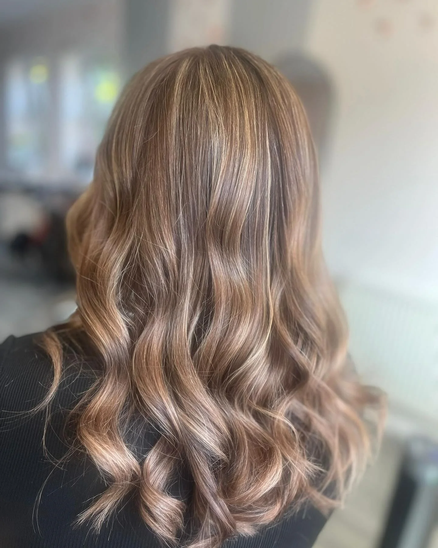 Back view of a woman with long, wavy, light brown hair with highlights, wearing a black top.
