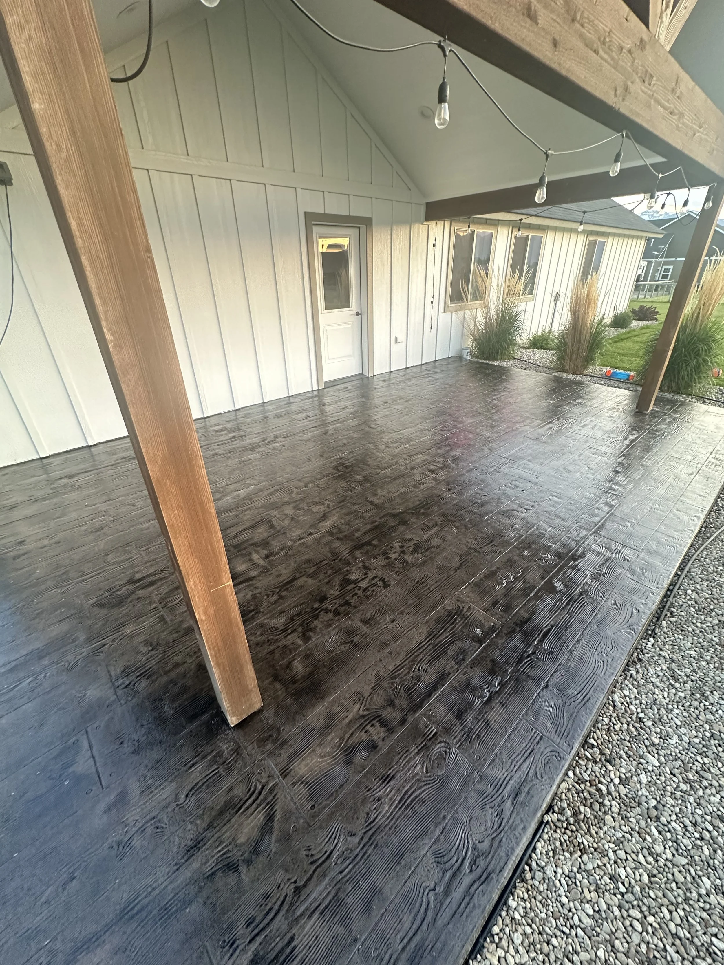 Back porch with black textured flooring, white paneling walls, and string lights hanging from a wooden frame