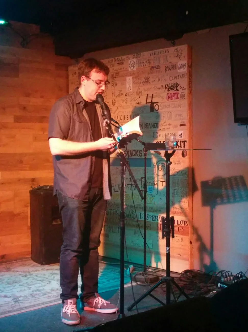 A person standing on a stage reading from a book into a microphone.