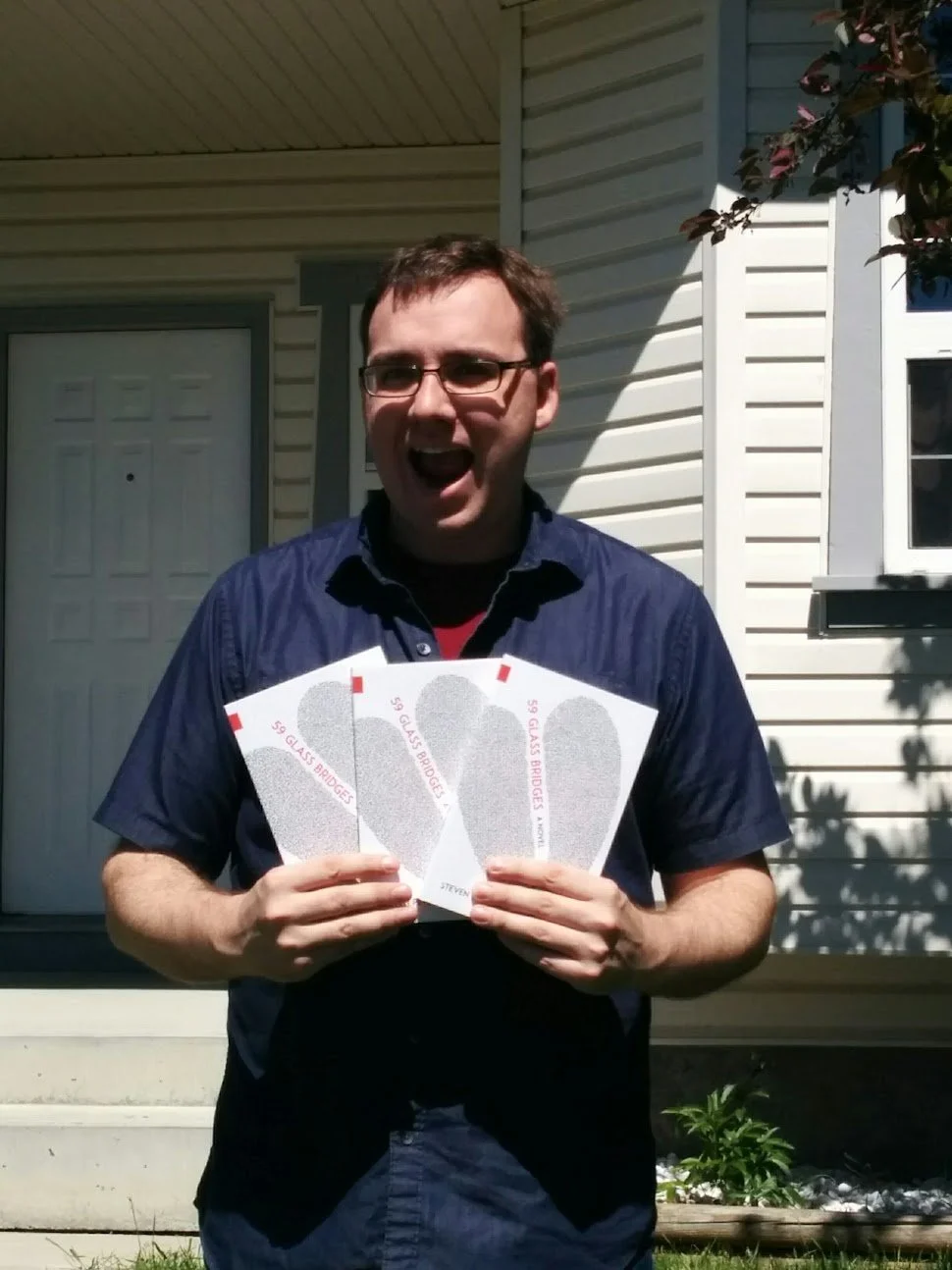 Man holding three tickets labeled '59 GLASS BRIDGES', smiling outside in front of a house.